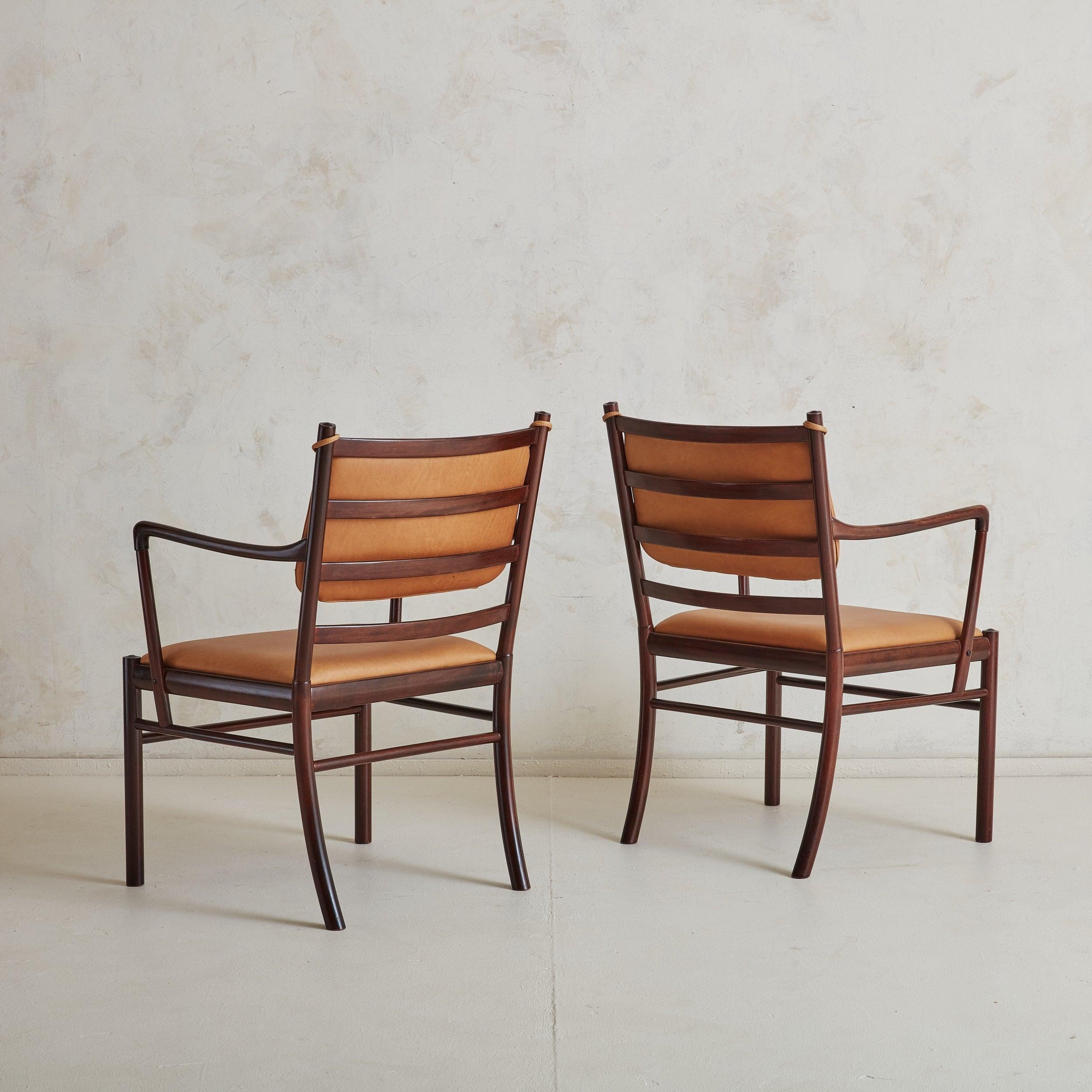 An elegant pair of Danish Modern ‘Colonial’ armchairs designed by Ole Wanscher in the 1960s. These armchairs feature slim mahogany frames in a polished burgundy finish, camel toned leather seats, and matching removable back cushions. A fantastic