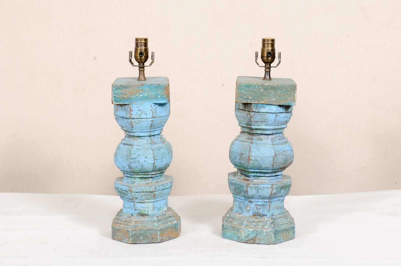 A pair of painted table lamps fashioned out of cut sections of old carved wood columns. This pair of lamps feature a thick central column, carved and turned with differing geometrical trimmings about the exterior, with a squared top, and raised on a