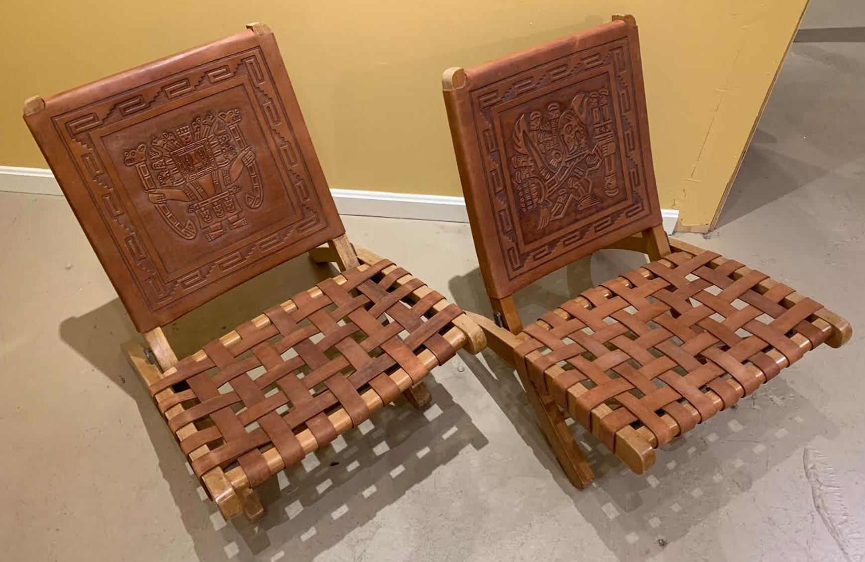 A fine pair of wood and leather folding chairs from Peru, decorated with tooled Aztec decoration on the leather backs, and include leather woven seats. The chairs date to the 1970s and are in very good overall condition, with minor imperfections and