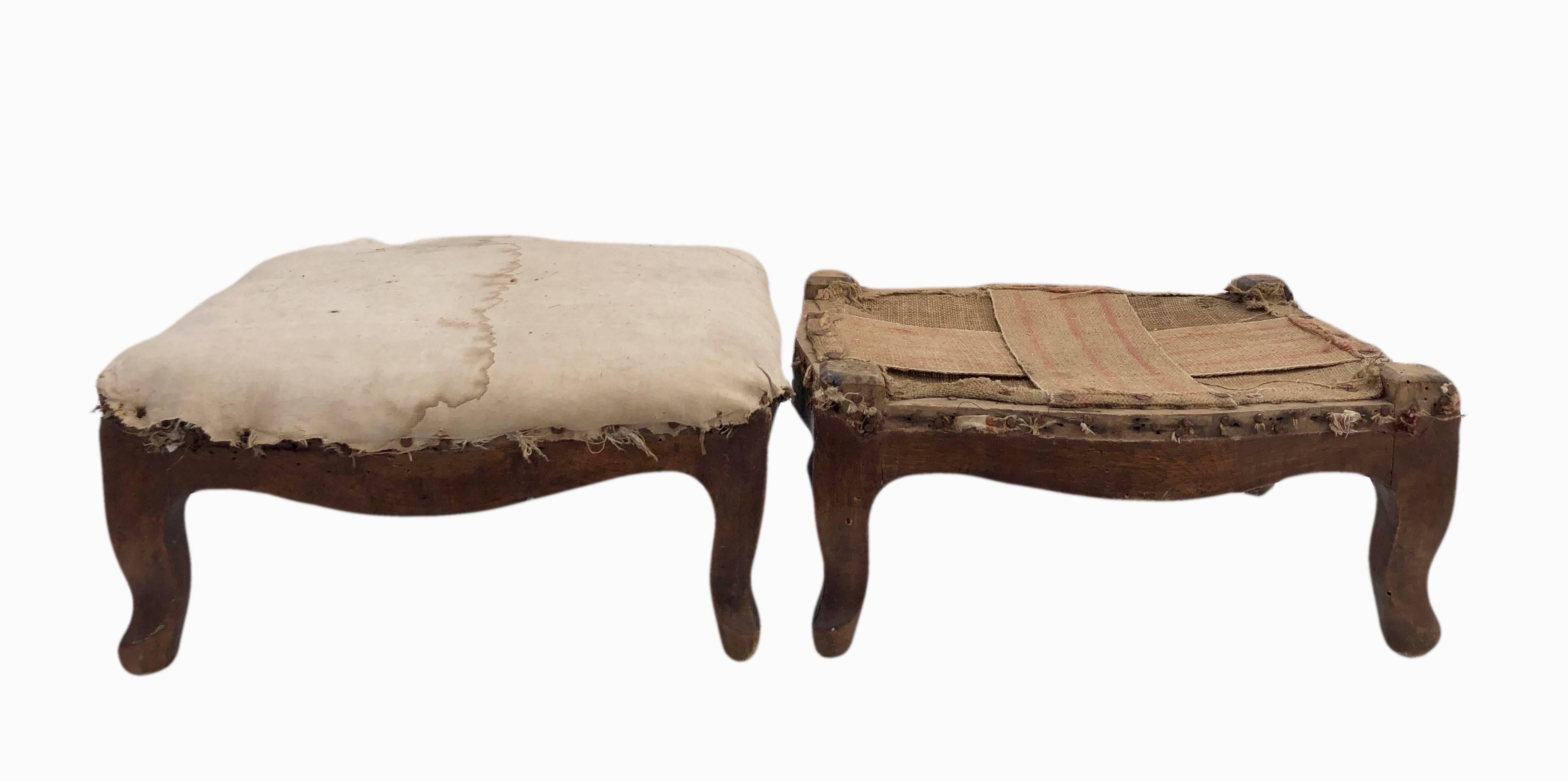 These are a beautiful pair of wooden French early 1800s footstools. One is straw filled with a white cotton cover while the other has its original banding. They are Regency footstools untouched in their original state with burlap covered bottoms.