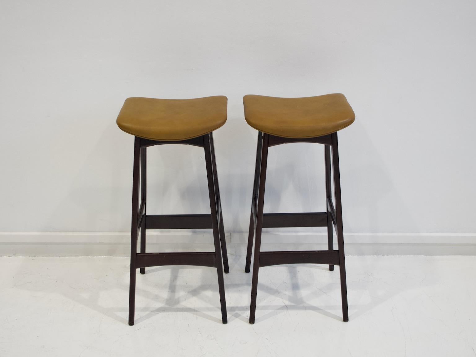 Two bar or kitchen stools with mahogany-covered beech frame, design attributed to Johannes Andersen. Seats upholstered in brown faux leather. Produced in Denmark, circa 1960s.