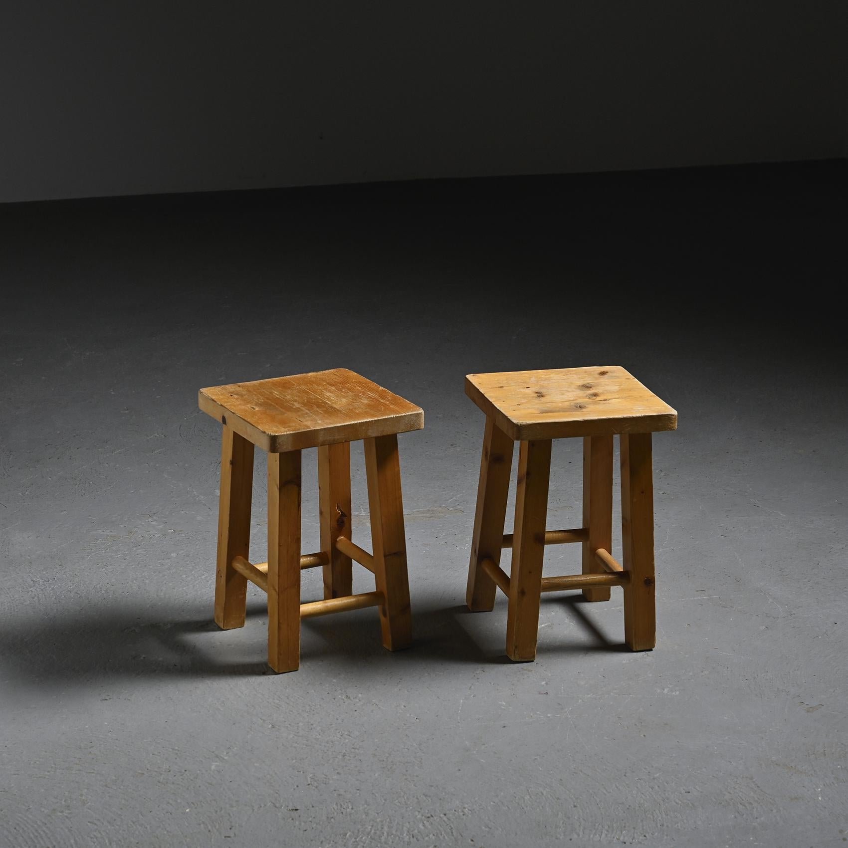 Pair of stools with four quadrangular legs joined by staggered cylindrical stretchers, creating a rhythmic structural balance. Designed by Charlotte Perriand, they are part of her comprehensive interior architecture and furnishing project for the La