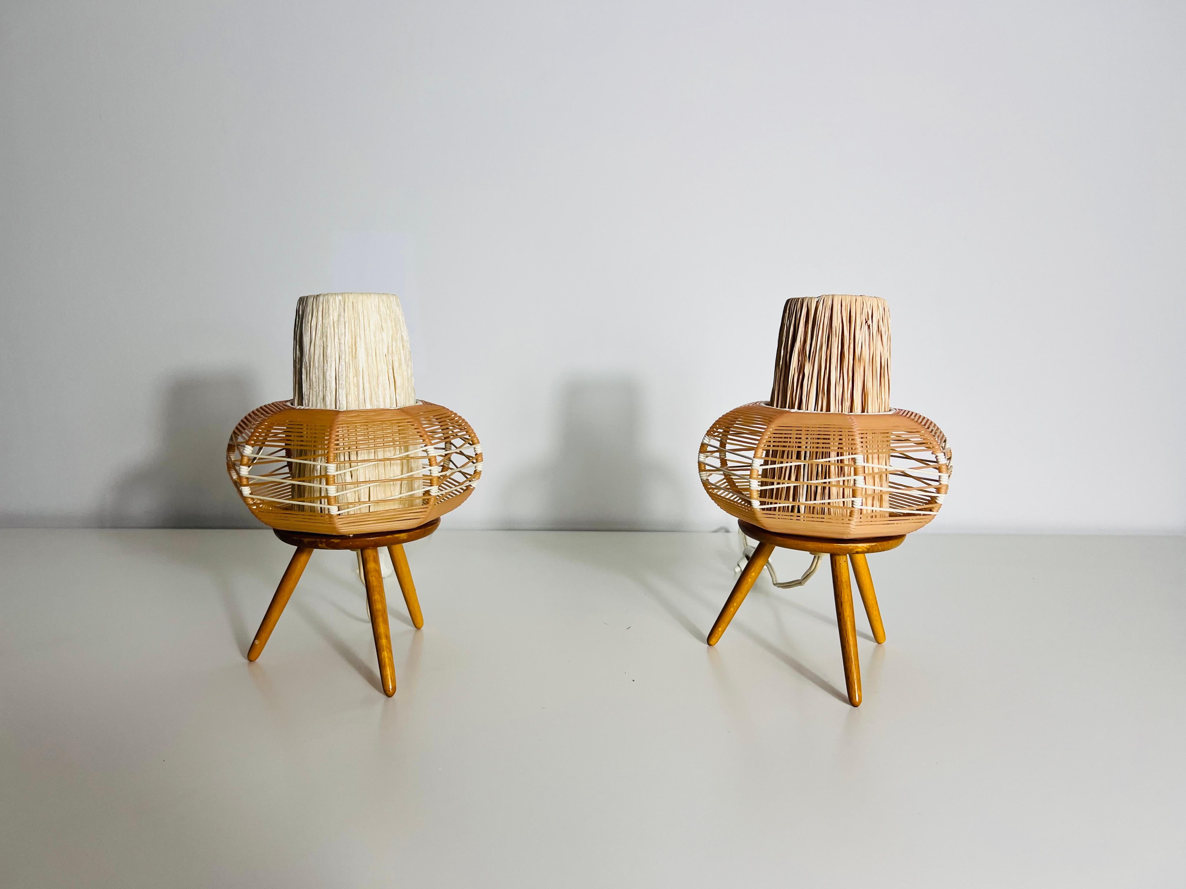 This pair of vintage table lamps showcases the timeless elegance of mid-century Swiss design from the 1970s. Featuring a combination of natural wood and intricately woven rattan, the lamps blend organic textures with minimalist shapes, making them a