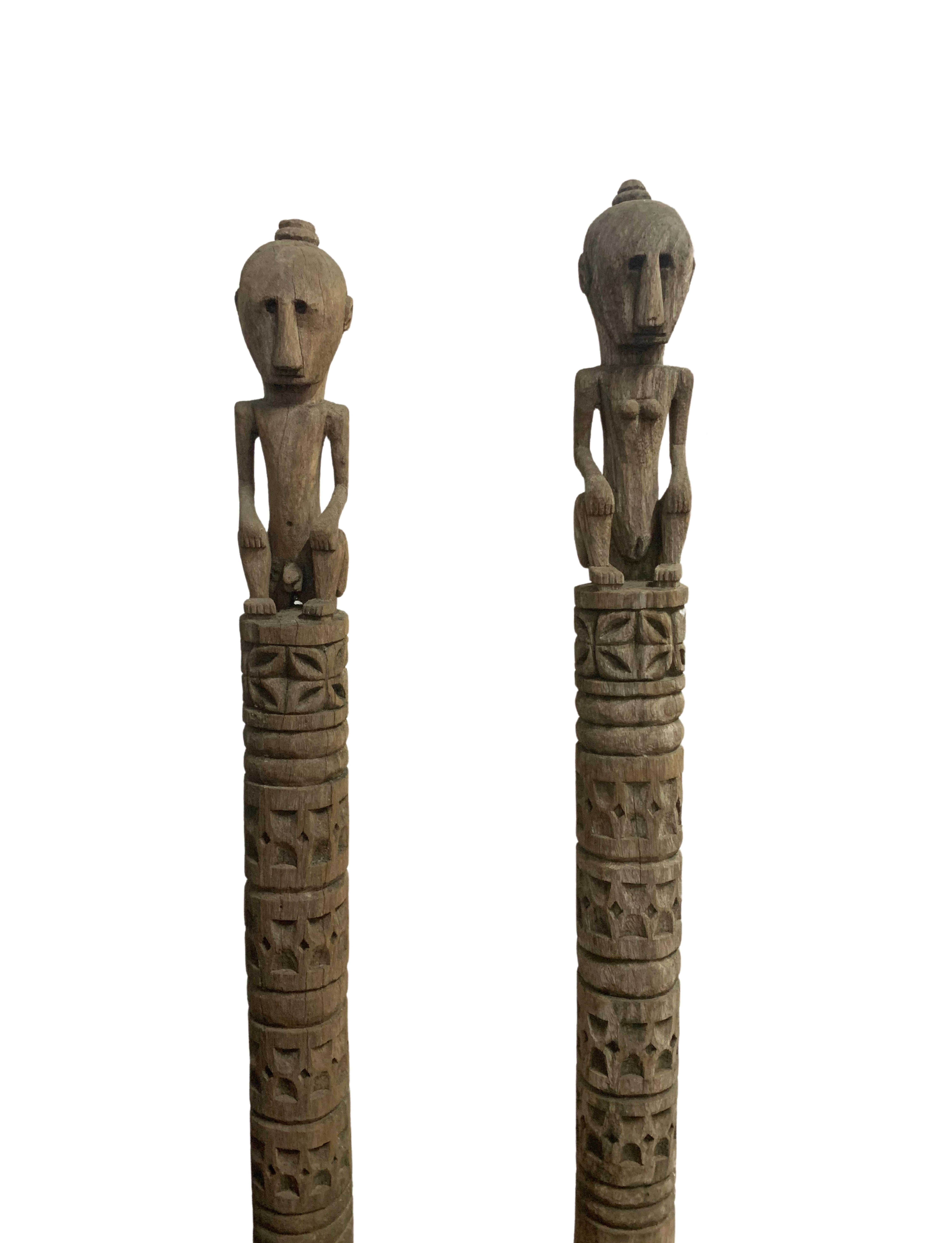 This pair of wooden sculpture of ancestral figures originate from the Island of Timor in Indonesia. They feature tribal engravings and feature a male and female figure. Carved from a single block of wood the sculptures are mounted on a black iron