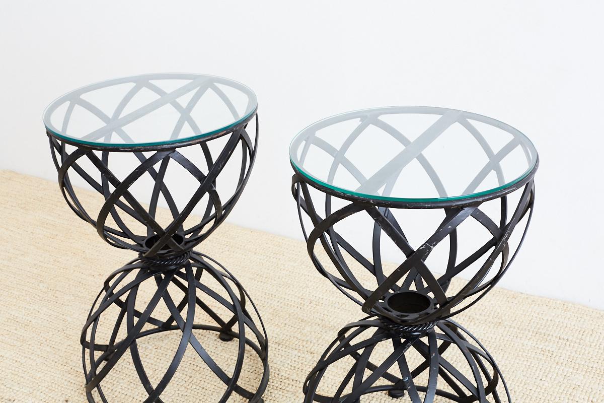 Amazing pair of wrought iron drink tables featuring a woven basket design. Each table constructed with a waisted form and a decorative faux rope belt in the middle. The basket ribbons connect to round rings on top and bottom. Finished with a pane of
