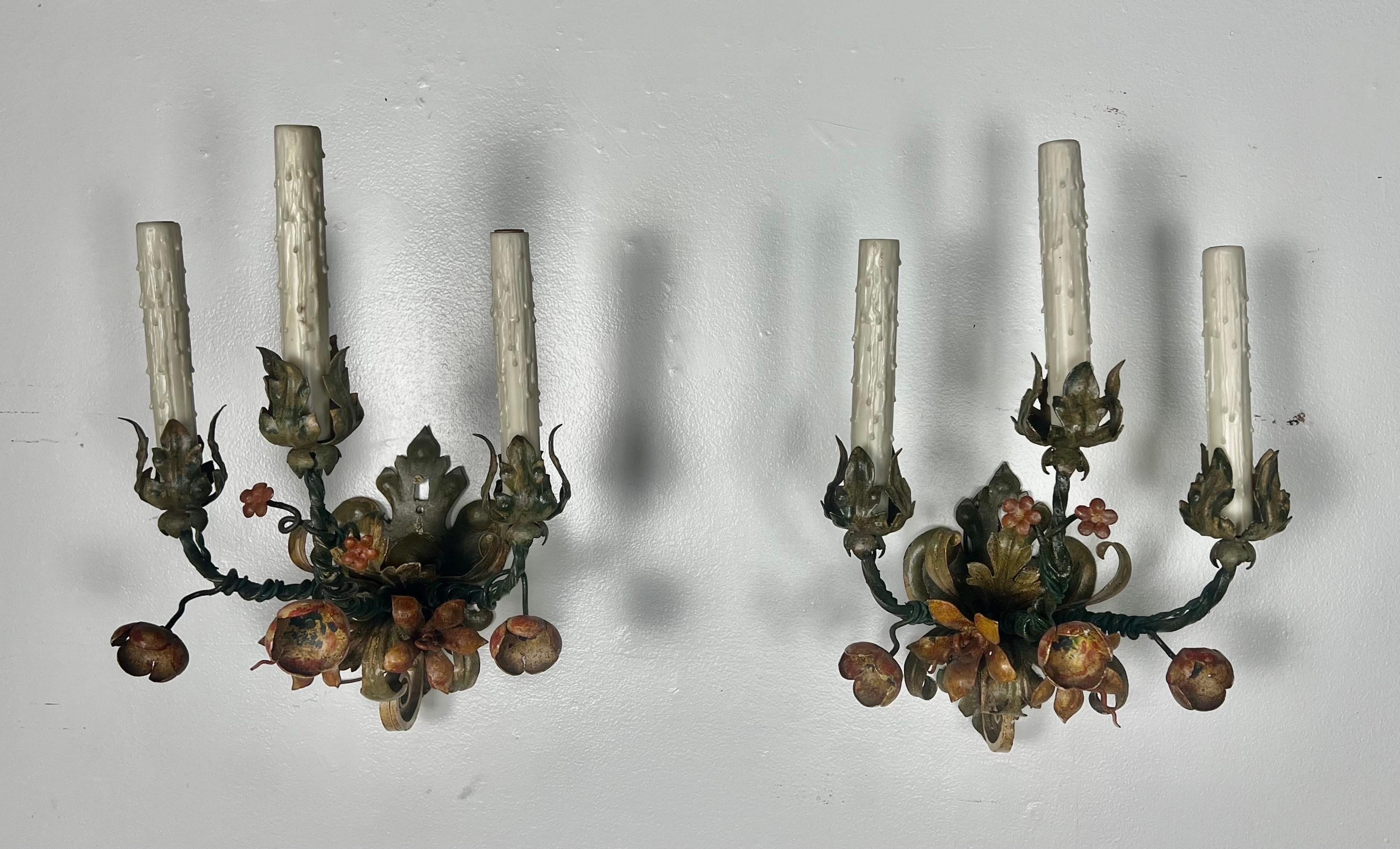 Pair of French 3-light wrought iron and painted sconces.  The sconces are adorned with flowers painted in shades of green and terra cotta.  The sconces are wired and in working condition.  Beautiful painted finish with bits of gilt metal underneath.