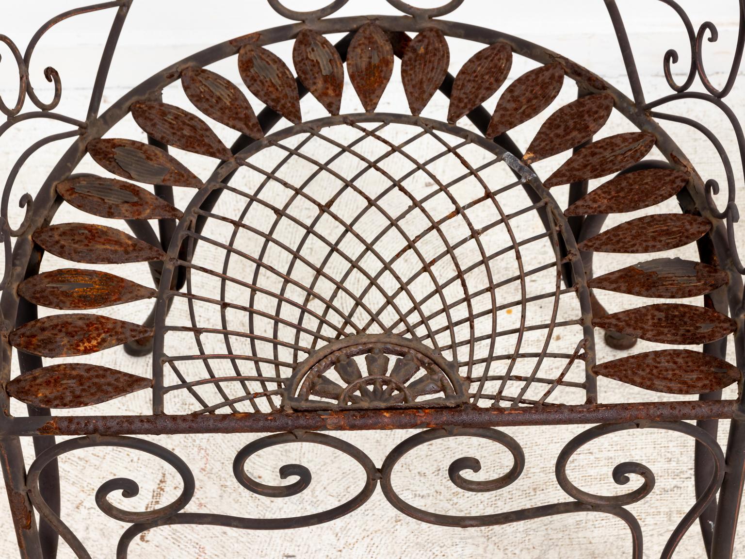 Pair of wrought iron curved back garden chairs with c-scroll detail on the seat back and front of the seat rail. The seat is further detailed with latticework and metal leaves in the shape of sunflower. Please note of wear consistent with age and