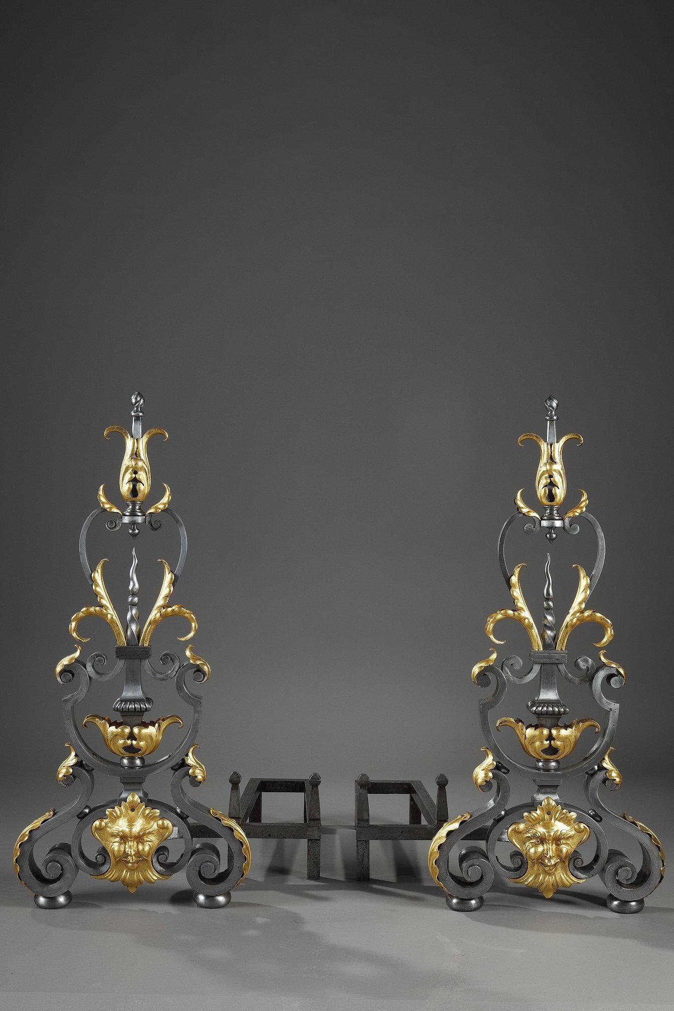 A large and beautiful pair of wrought-iron landiers or mantel fronts decorated with scrolls and foliage enhanced with gold, with a mask at the bottom. The contrasting colors underline the decorative character. The andirons come with their iron to