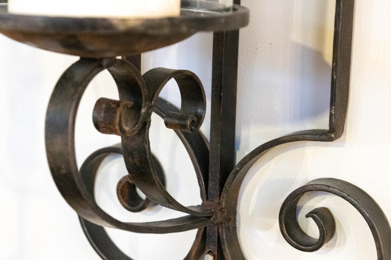 Pair of wrought iron wall sconces with newly purchased glass hurricane cylinders and candles. Both are removable. There are two holes in rod that allow for attachment to wall.