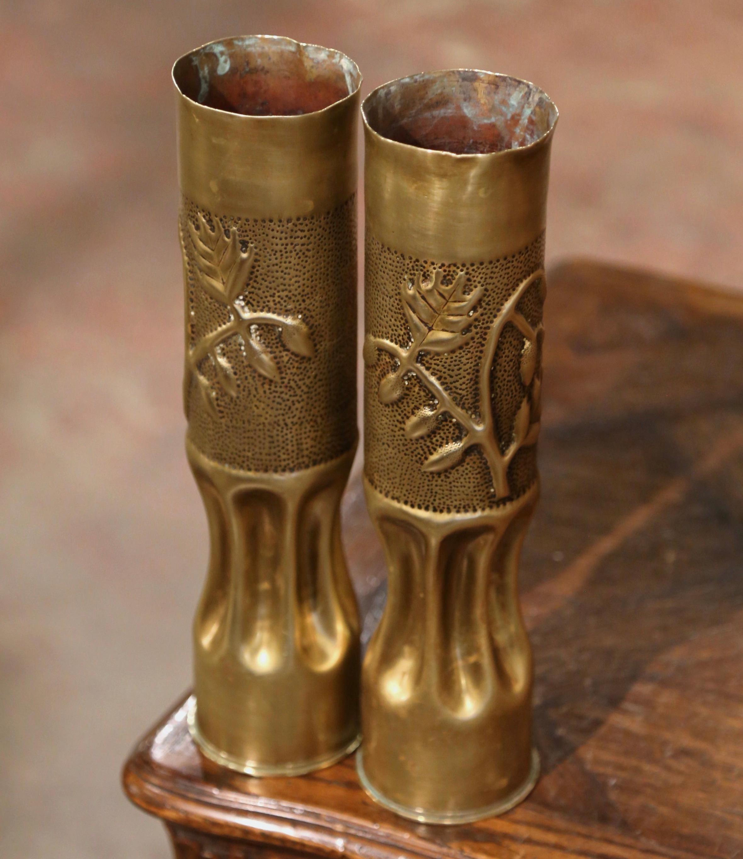 Decorate a man's office or a study display shelf with this pair of antique trench art shell casings. Created in France, and dated 1916, each artillery shell is made of brass, and features repousse floral and leaf decor over a top rim. The tall WWI