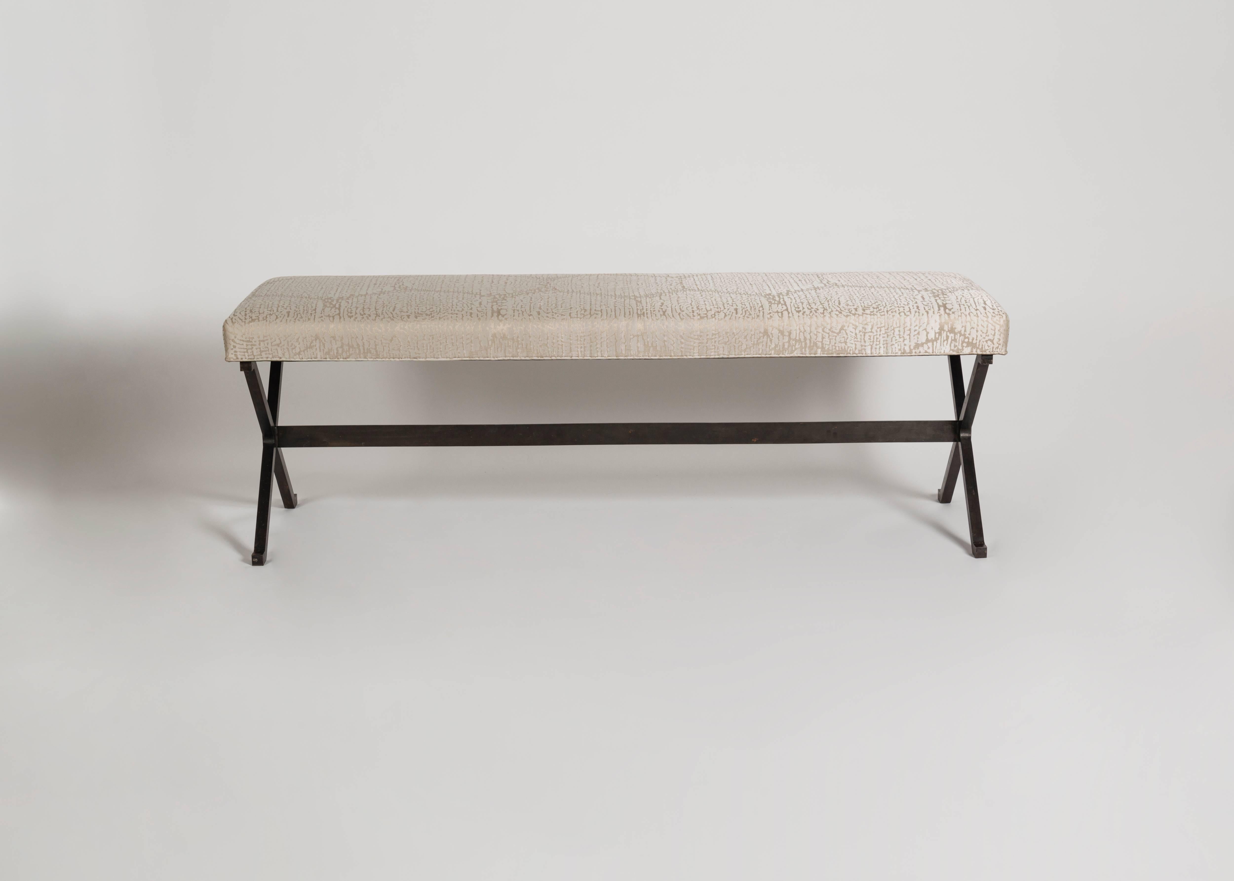 A pair of long cushioned benches, each with a patinated steel base in the form of twin Xs supported by a cross bar.