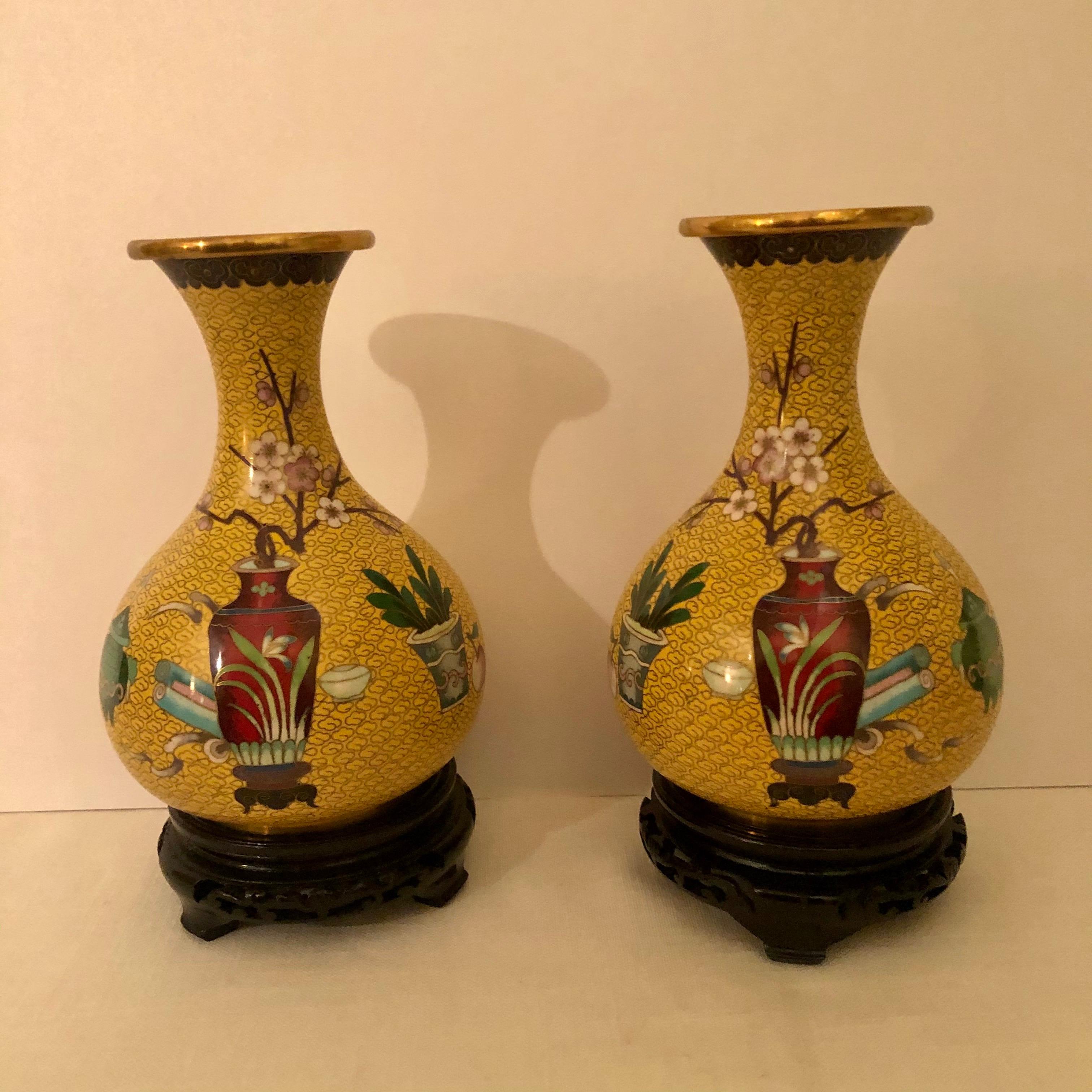 This is a pair of wonderful yellow ground Chinese cloisonné vases. They are each decorated with a red Chinese vase holding Prunus flowers. This decoration stands out against the yellow ground with the cloud decorations all over the vases. They come