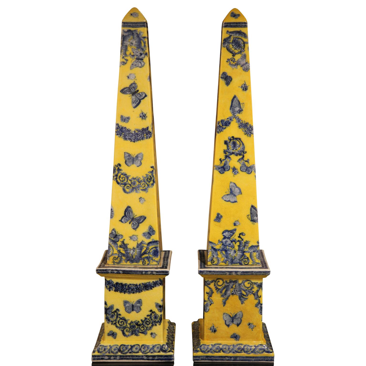 Pair of bright yellow obelisks with cobalt blue butterflies and flowers. The pair is identical with alternating designs on each face.