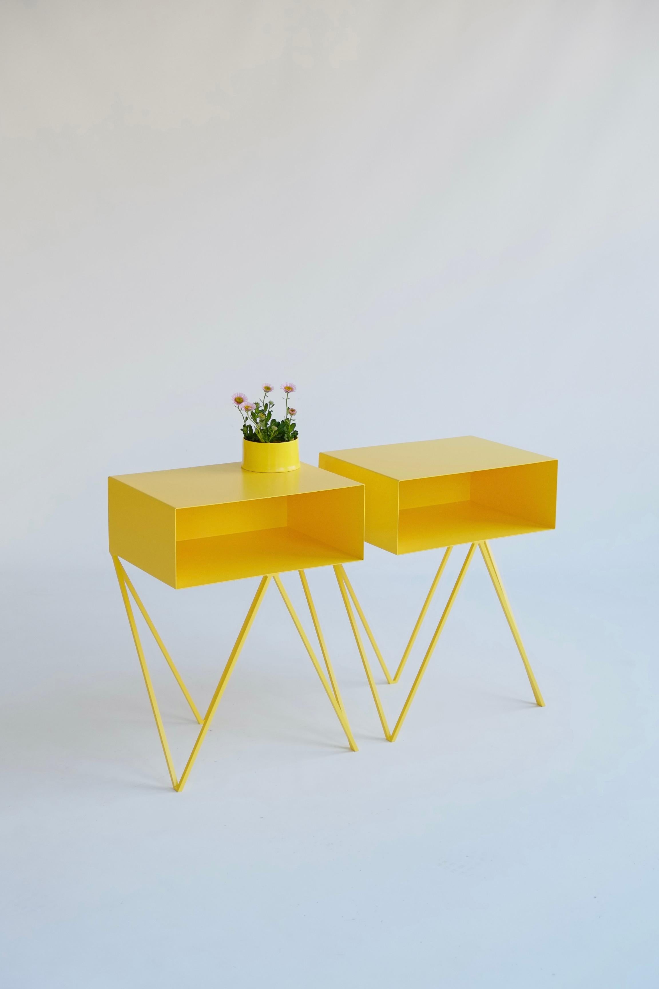 A pair of yellow Robot bedside tables. The Robot side table features an open shelf on zig zag legs. A fun and functional design made of solid steel, powder-coated in red. The clean lines look great against period details as well as in modern spaces.
