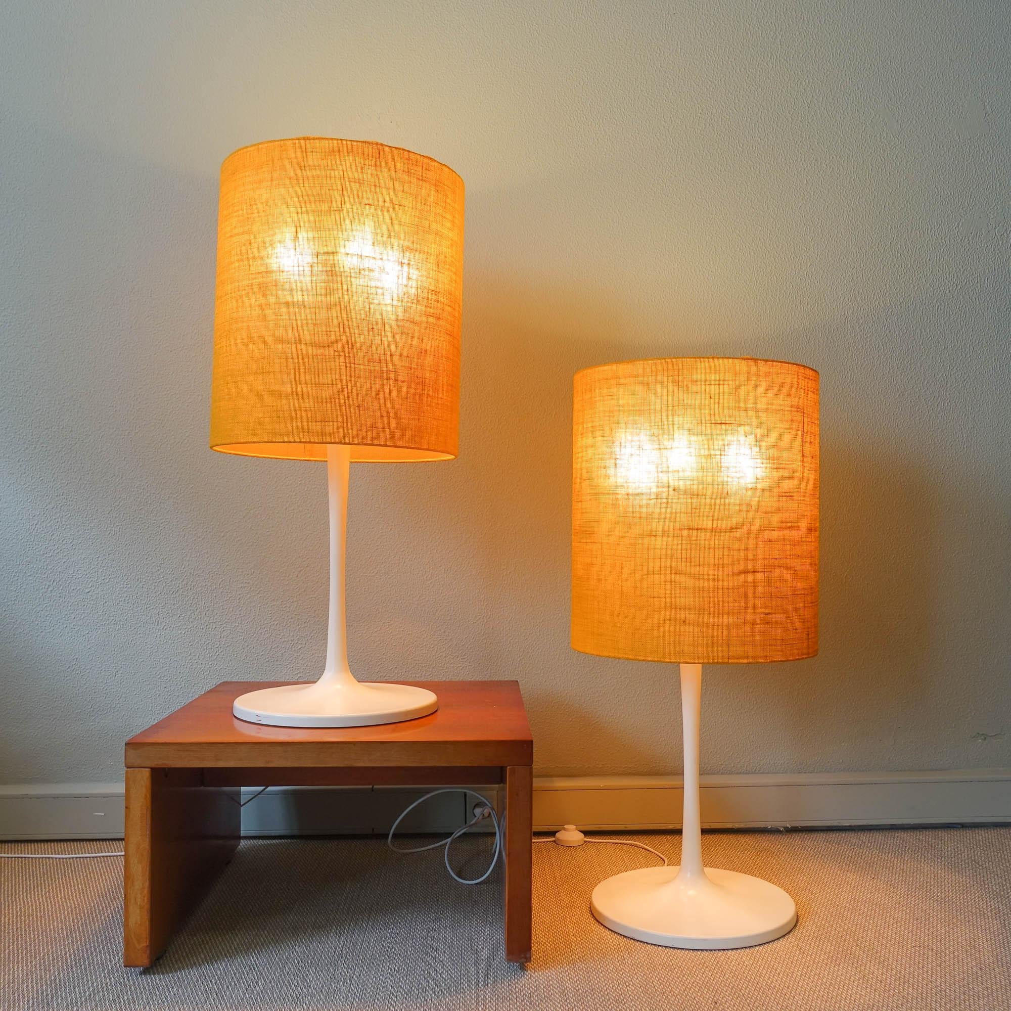 This pair of floor/ table lamps was designed and produced by Staff, in Germany, during the 1970's. Each lamp features a white lacquered metal tulip feet and cylindrical shades made of plastic coated with yellow fabric. The light can be switched on