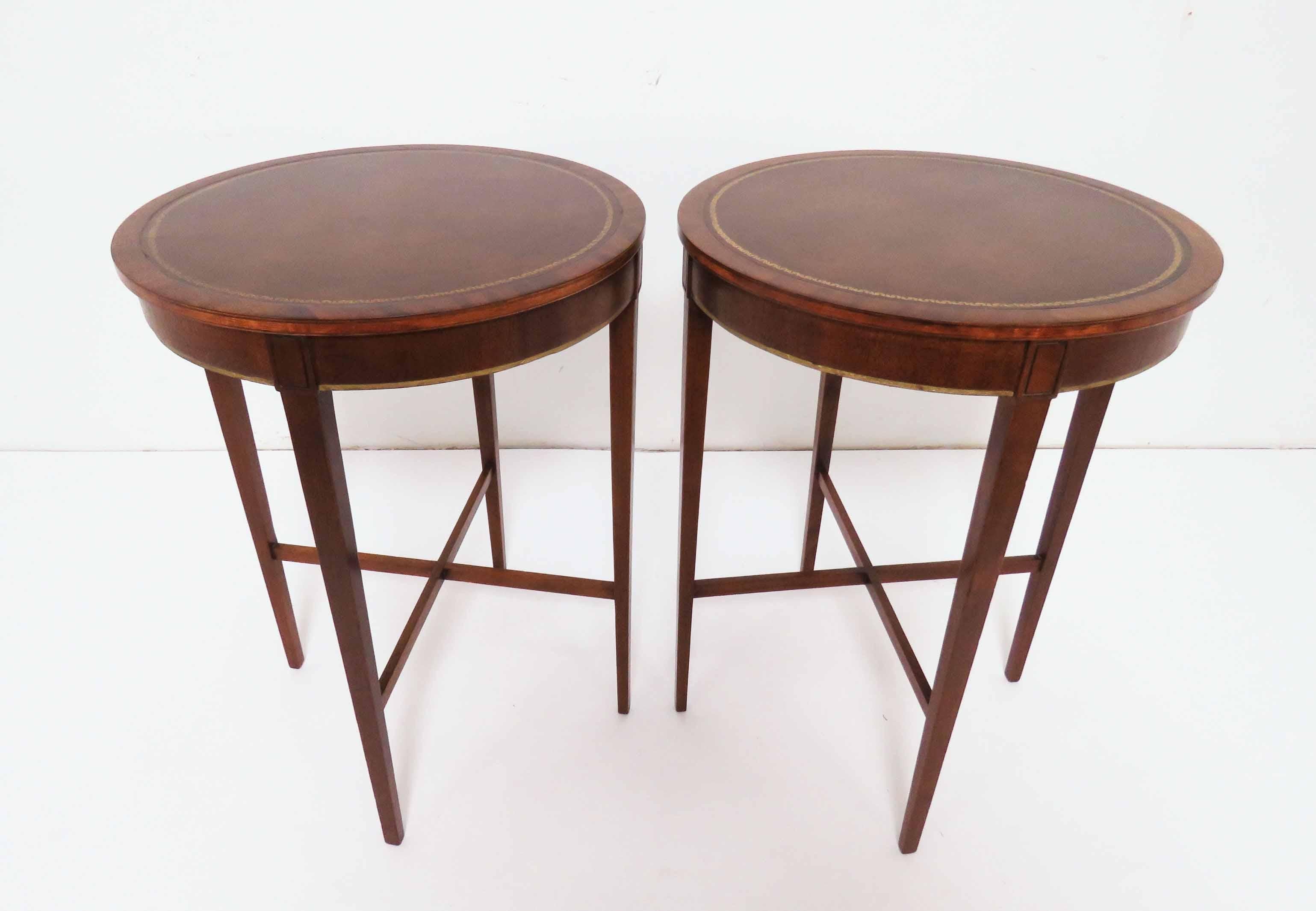 Pair of elegant midcentury lamp tables in mahogany with cross form stretchers and leather tops with embossed gilding, by the renowned firm of Zangerle & Peterson, Chicago, circa late 1940s.