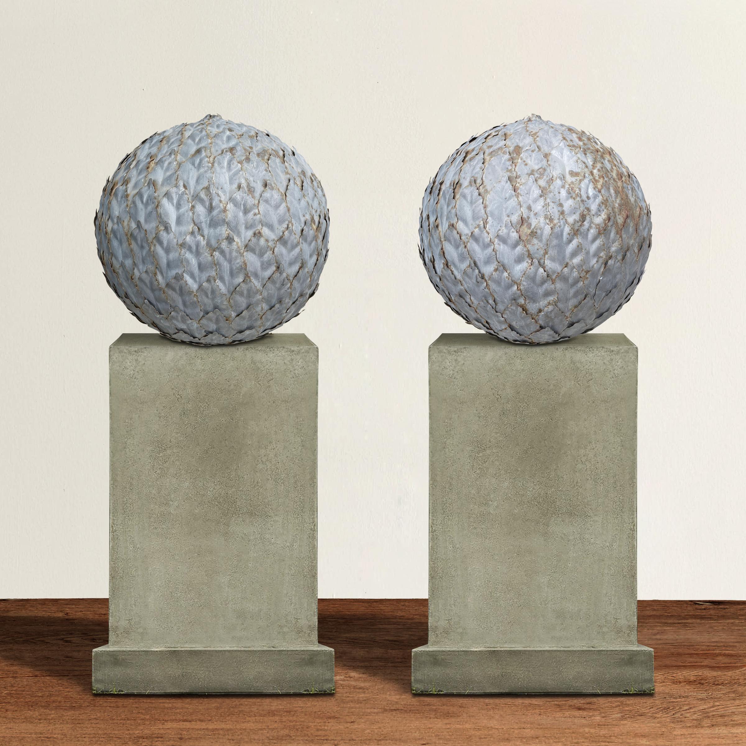 A wonderfully charming pair of 20th century English zinc garden spheres covered in laurel leaves and perfect for topping the columns flanking your driveway, placed along your garden path, or bring them indoors for a striking sculptural moment.