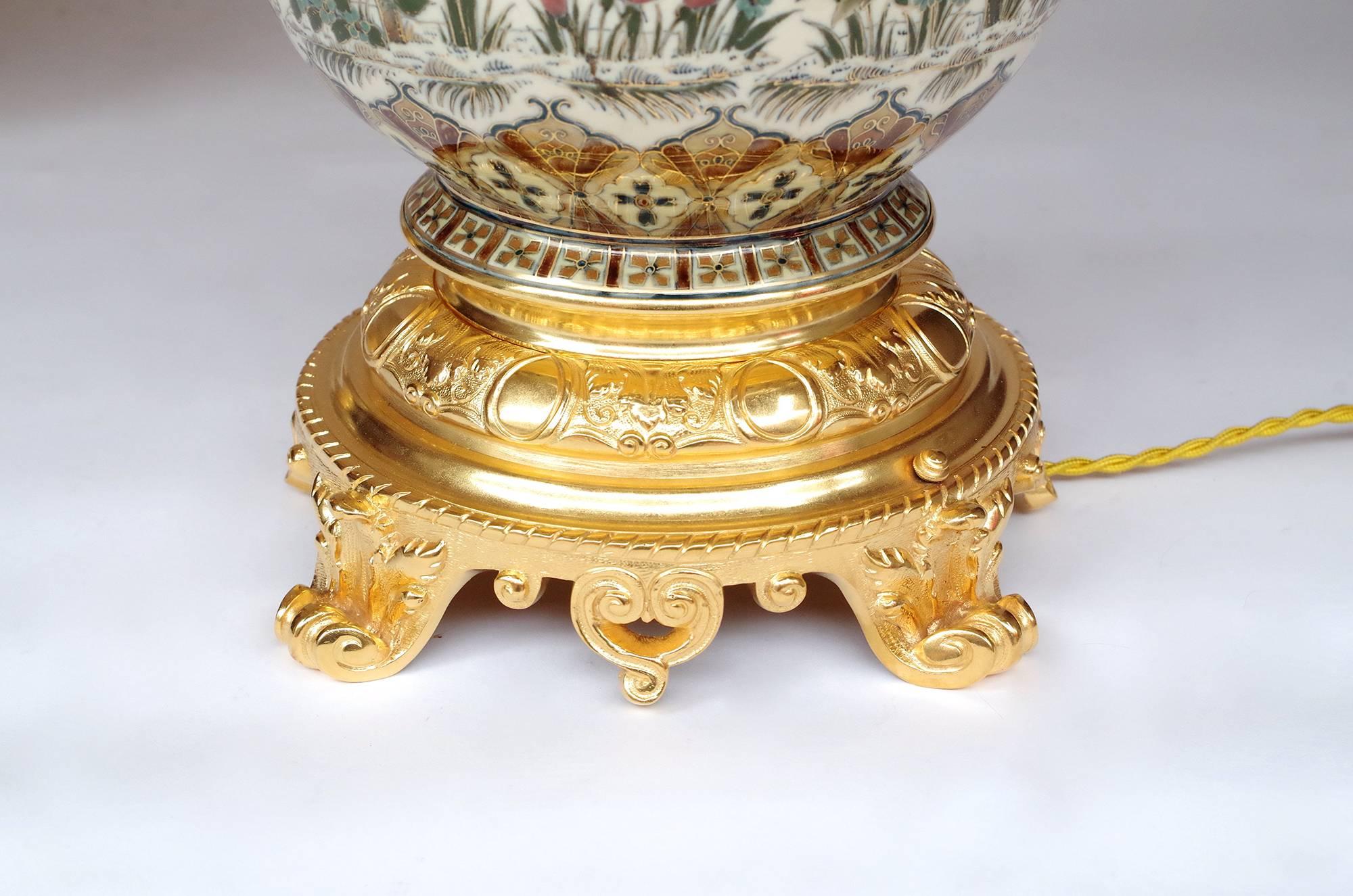 Pair of baluster shaped lamps in Zsolnay porcelain mounted in gilt bronzes.
Cream background decorated with birds, vegetals and flowers patterns, adorned with two friezes of stylized palm-leaves on the upper and lower parts of the body lamp with