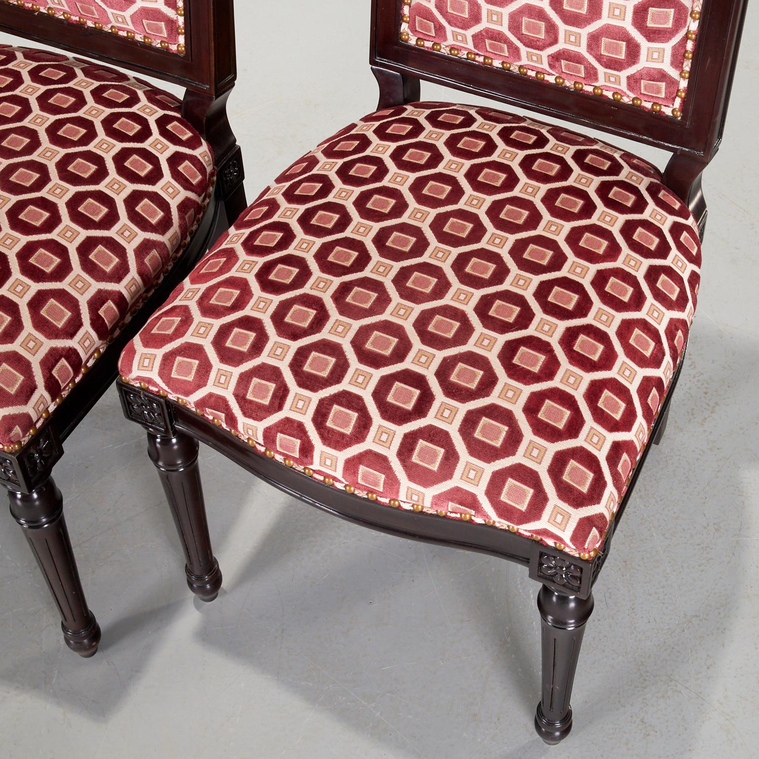 21st C., a pair of Oly side chairs with sculpted geometric pattern upholstery, nailhead trim, and lacquered hand carved hardwood frames. The upholstery is in a raspberry red colorway with hints of beige and pink on a cream ground. The side welting