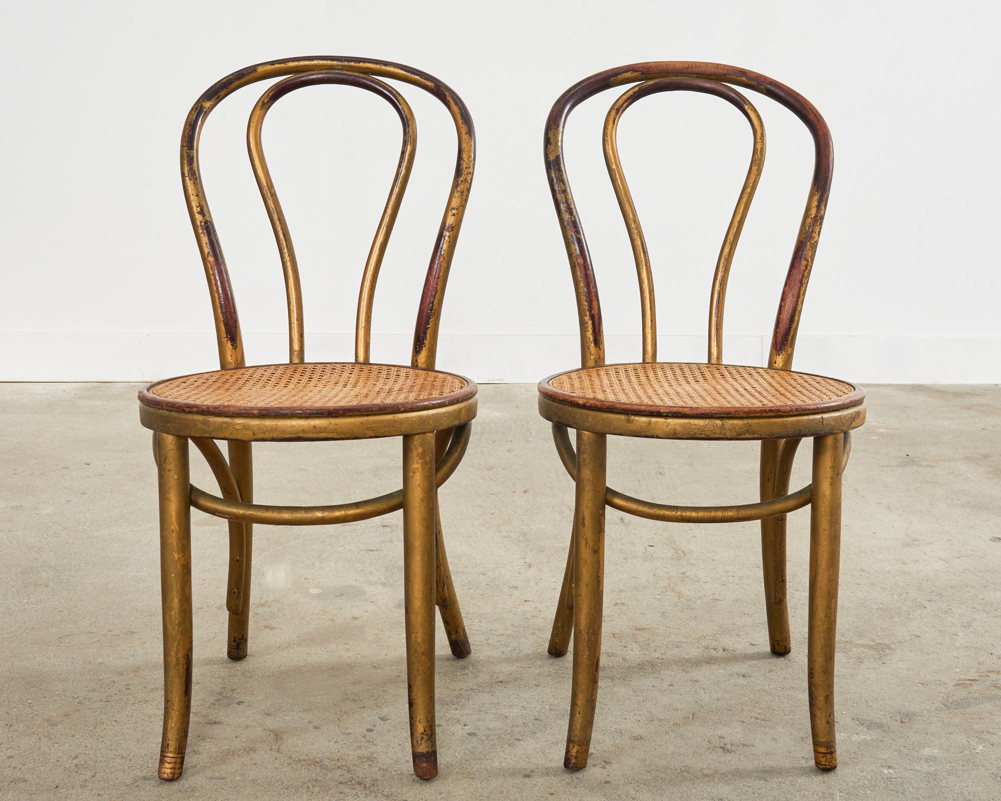 Iconic pair of Vienna secession period bistro dining chairs by Thonet. The No. 18 chair features a bentwood beech frame with a gracefully curved back conjoined to a round seat inset with cane. The chairs have a desirable aged, weathered patina with