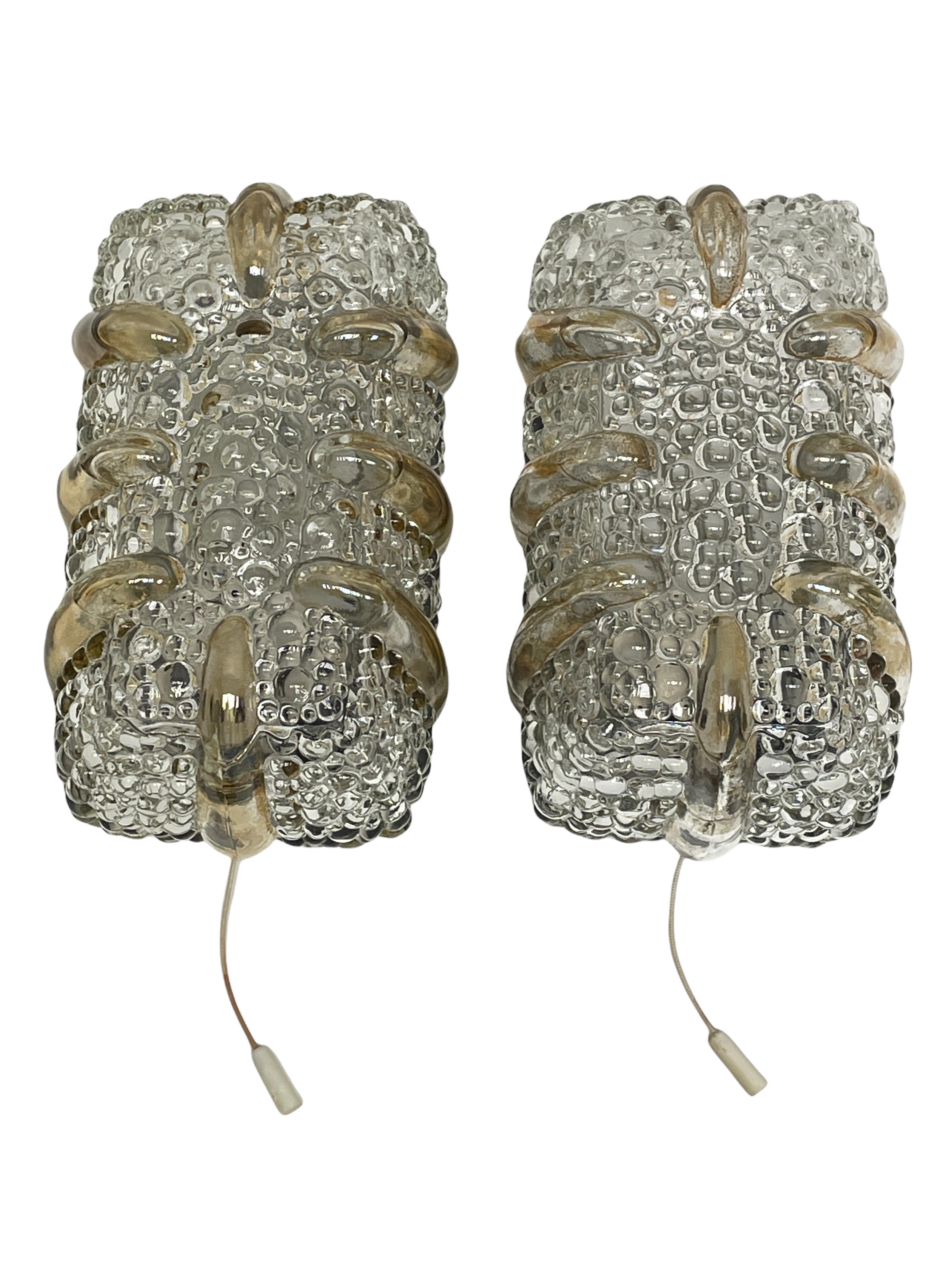 Pair of beautiful wall lights, made by Massive Leuchten, in textured glass, affixed against a metal socket with black lacquered base, circa 1970s. An iconic design from the 1970s and still relevant today. Good condition, consistent with age and use.
