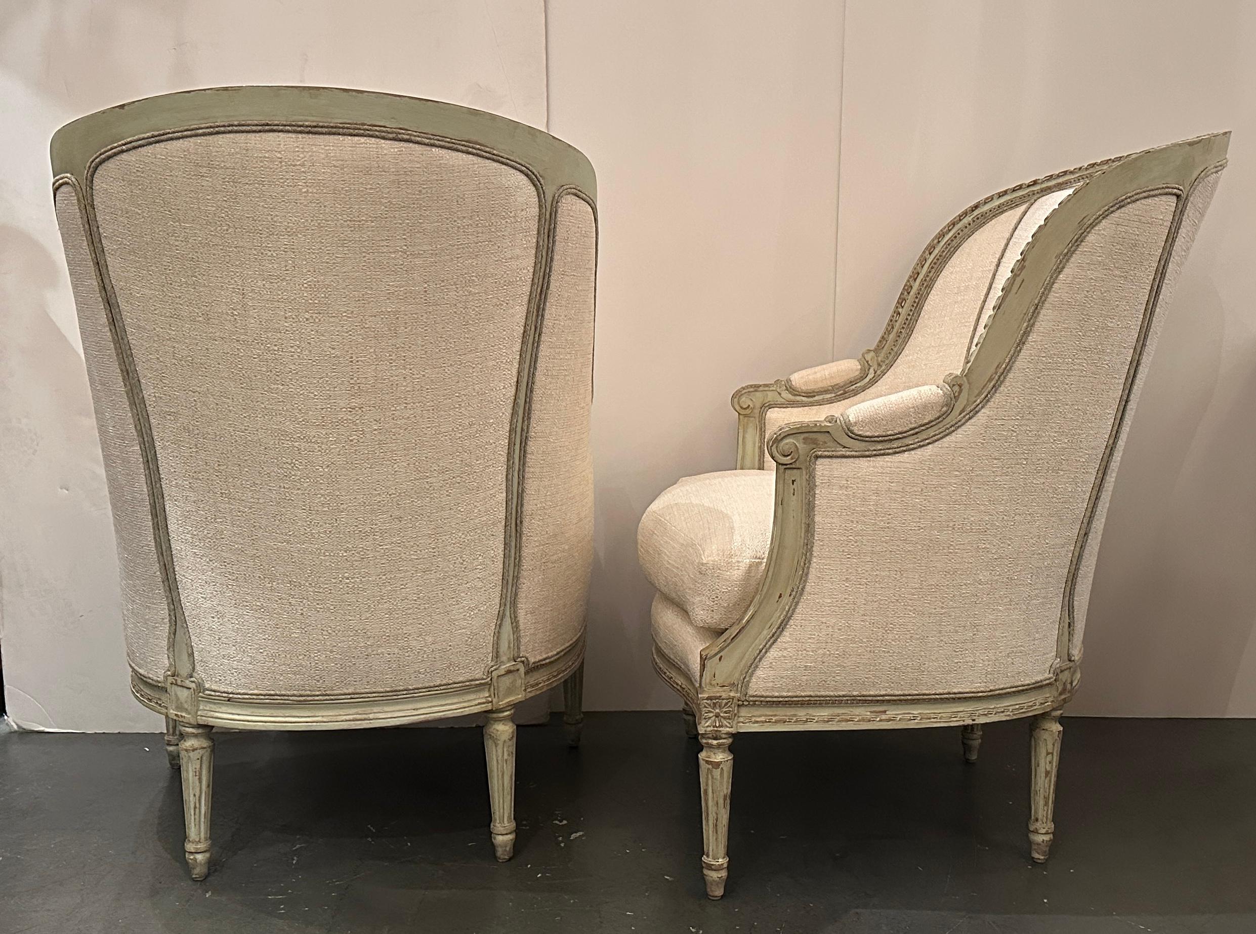 Pair of beautifully hand-carved and hand-painted Louis XVI style bergères with new off white textured upholstery with contrast fabric covered welting. 