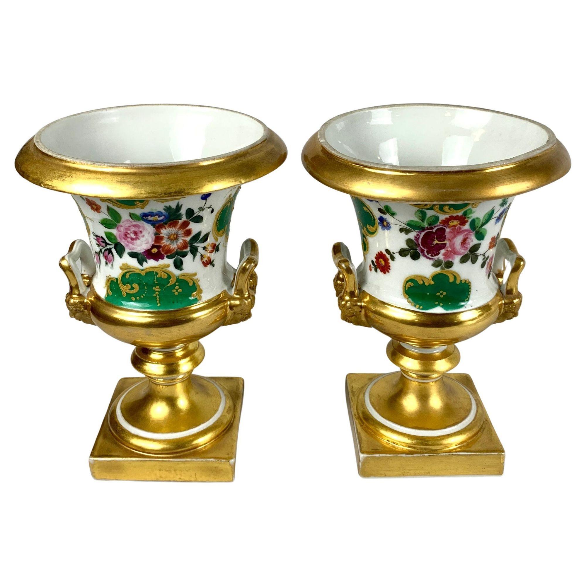 This pair of French Paris Porcelain mantle urns is decorated with hand painted flowers.
Crafting these urns circa 1840, the artist used enamels and gilt on white porcelain.
We see pink roses and other flowers painted in purple, orange and blue, and