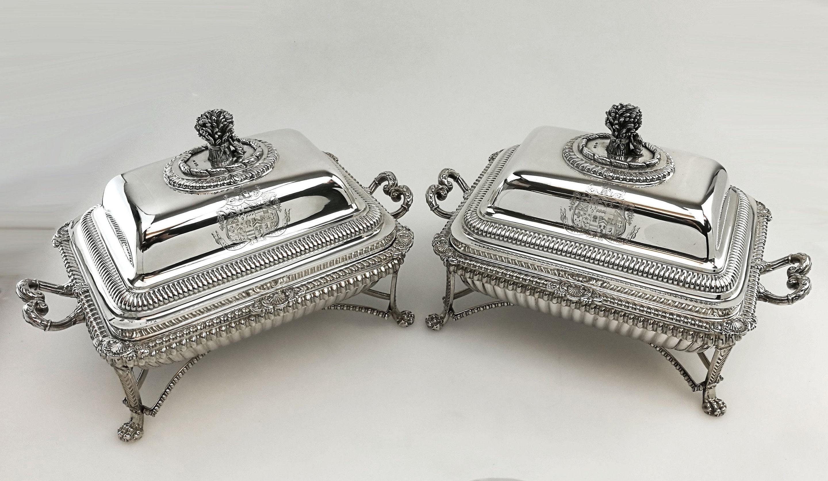 A spectacular pair of antique George III Paul Storr solid silver entree dishes on separate Sheffield plate warming stands. The sterling silver entree dishes feature a base with an impressive shell and gadroon border and a fitted lid with a tall