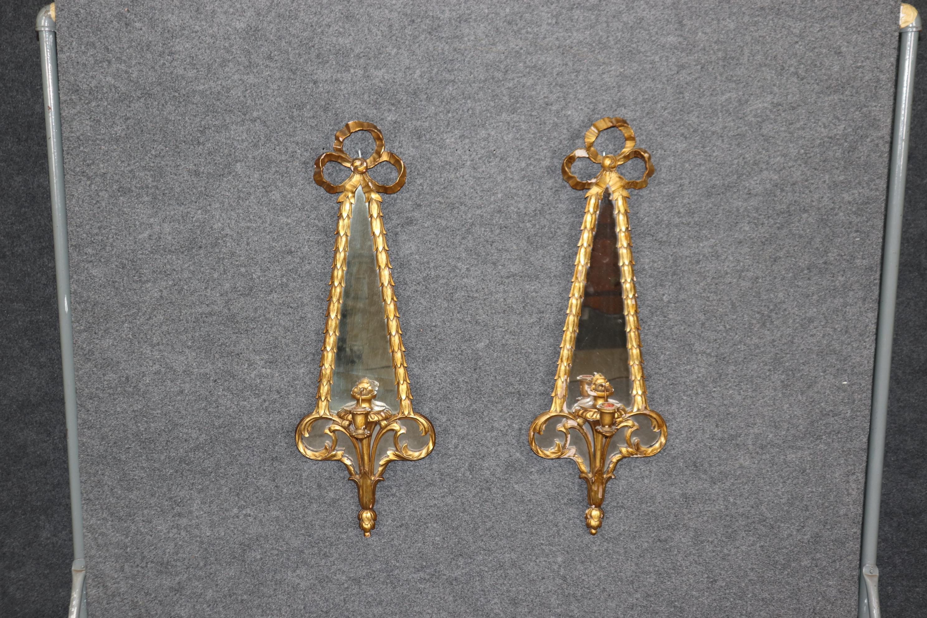 This is a stunning pair of single candle non-wired sconces. They can be wired by an electrician if desired. The sconces are time-worn with minor chips and signs of age and use. The sconces feature a bow and olive leaf motif that is very classic and