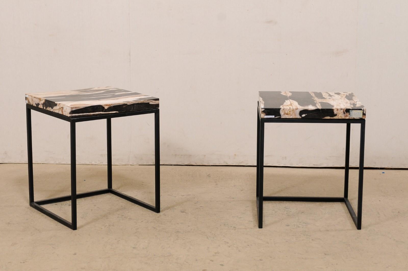 A pair of modern style custom created petrified wood top and iron side tables. This pair of tables each feature a square-shaped petrified wood top, in shades of black, tan, and off-white. The tops are supported by a custom metal base, which is black