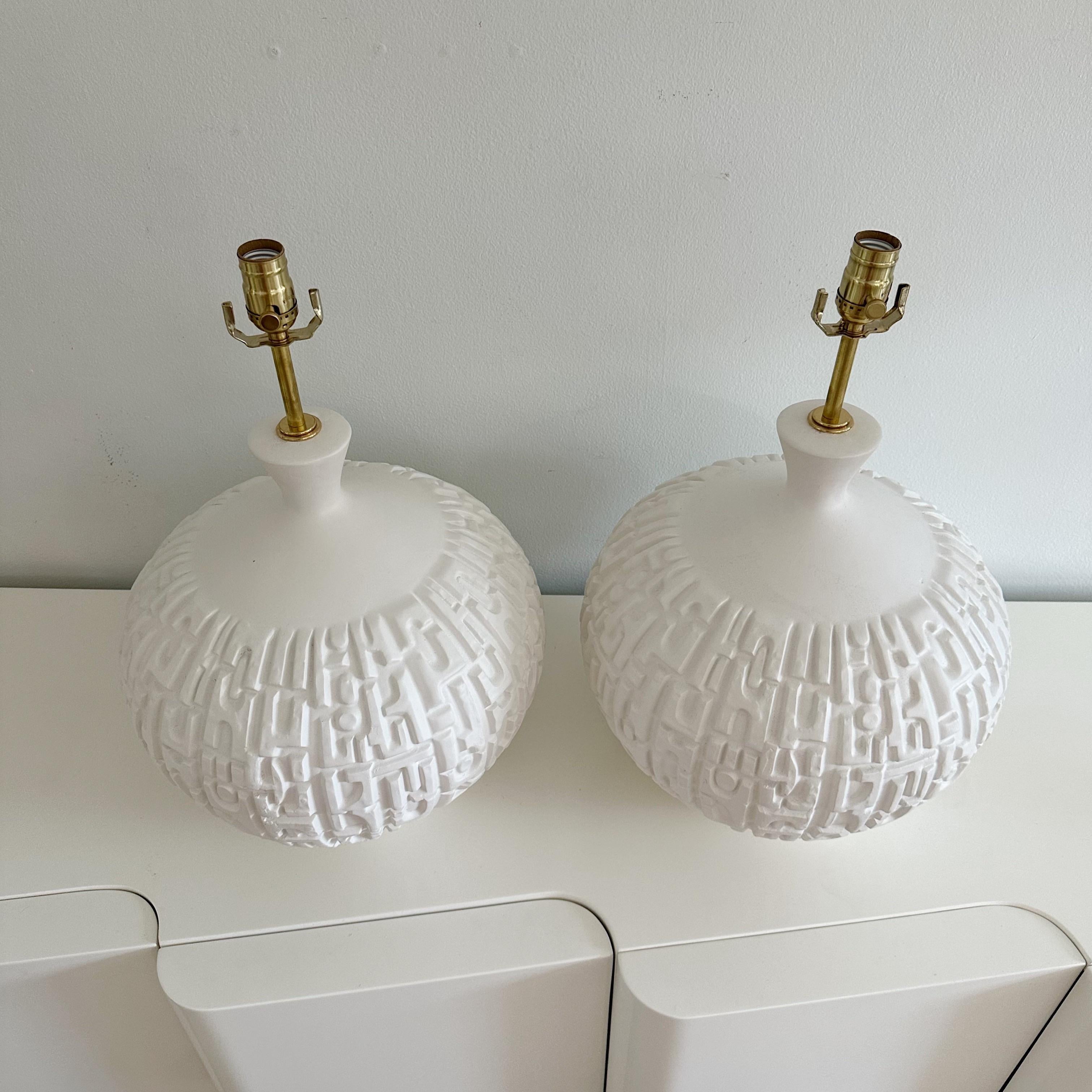 Substantial round plaster lamps from the 1970s, Featuring textured, incised, geometric brutalist design that adds a touch of artistic intrigue. Professionally rewired with a white silk cord and solid brass fittings. These lamps seamlessly blend