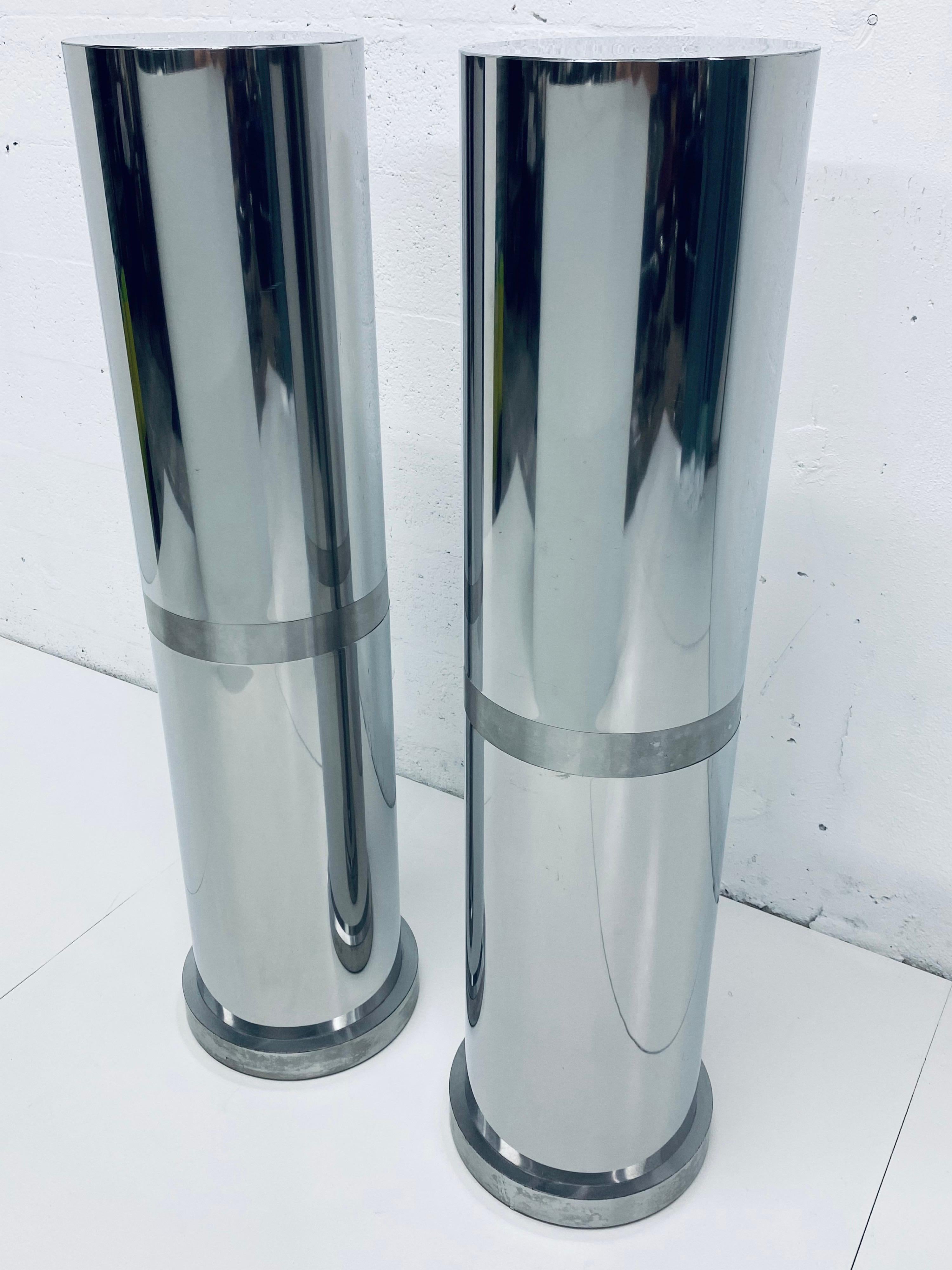 Two polished steel tall round pedestal tables or columns with brushed steel banding and chrome rivets from the 1970s.

Measures: Surface diameter: 12