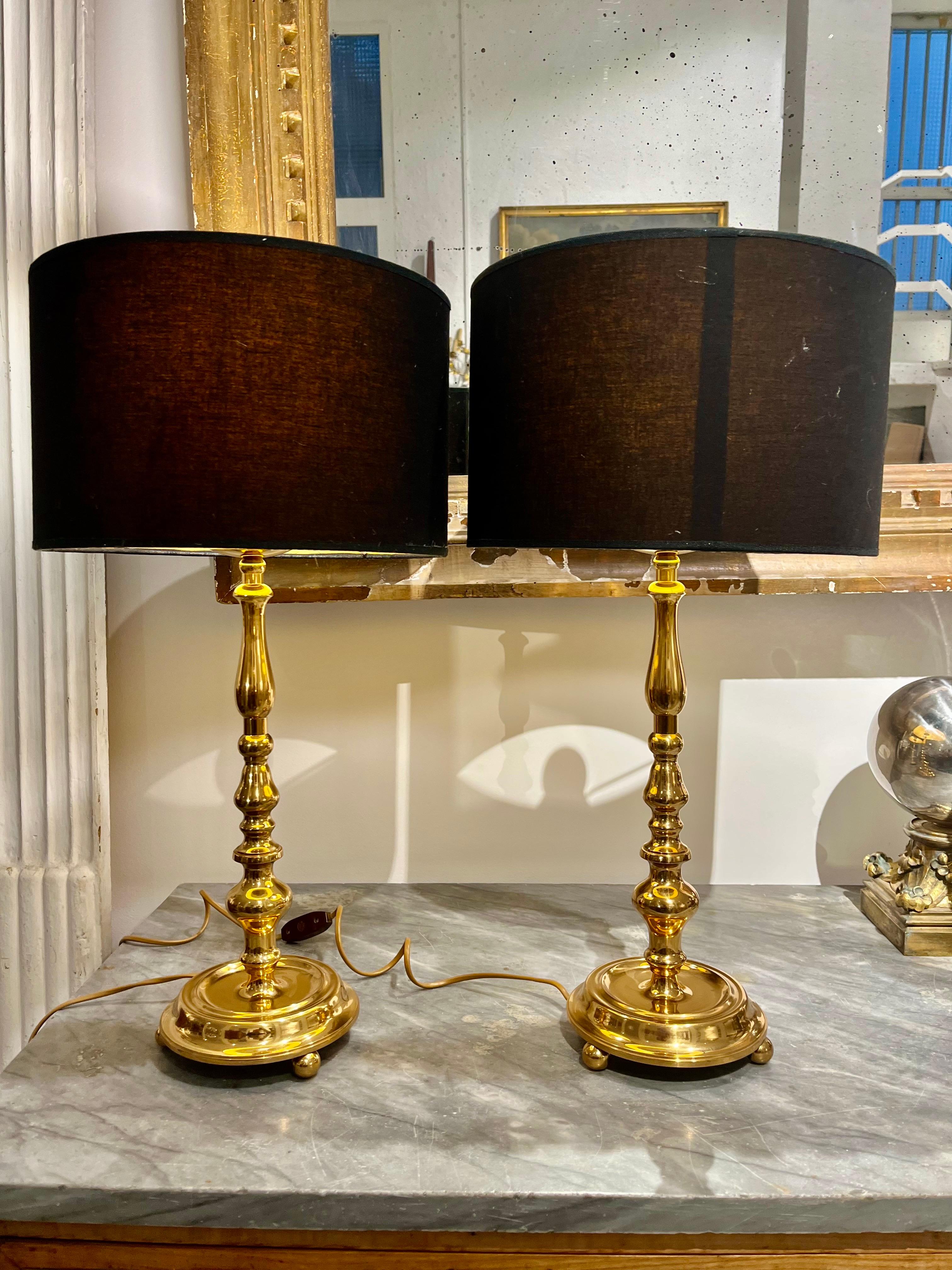 A pair of Swedish lamps, in Renaissance style in solid and polished brass, round base supported by brass balls, are prepared for use in the US, the lampshades is black with  gold interior