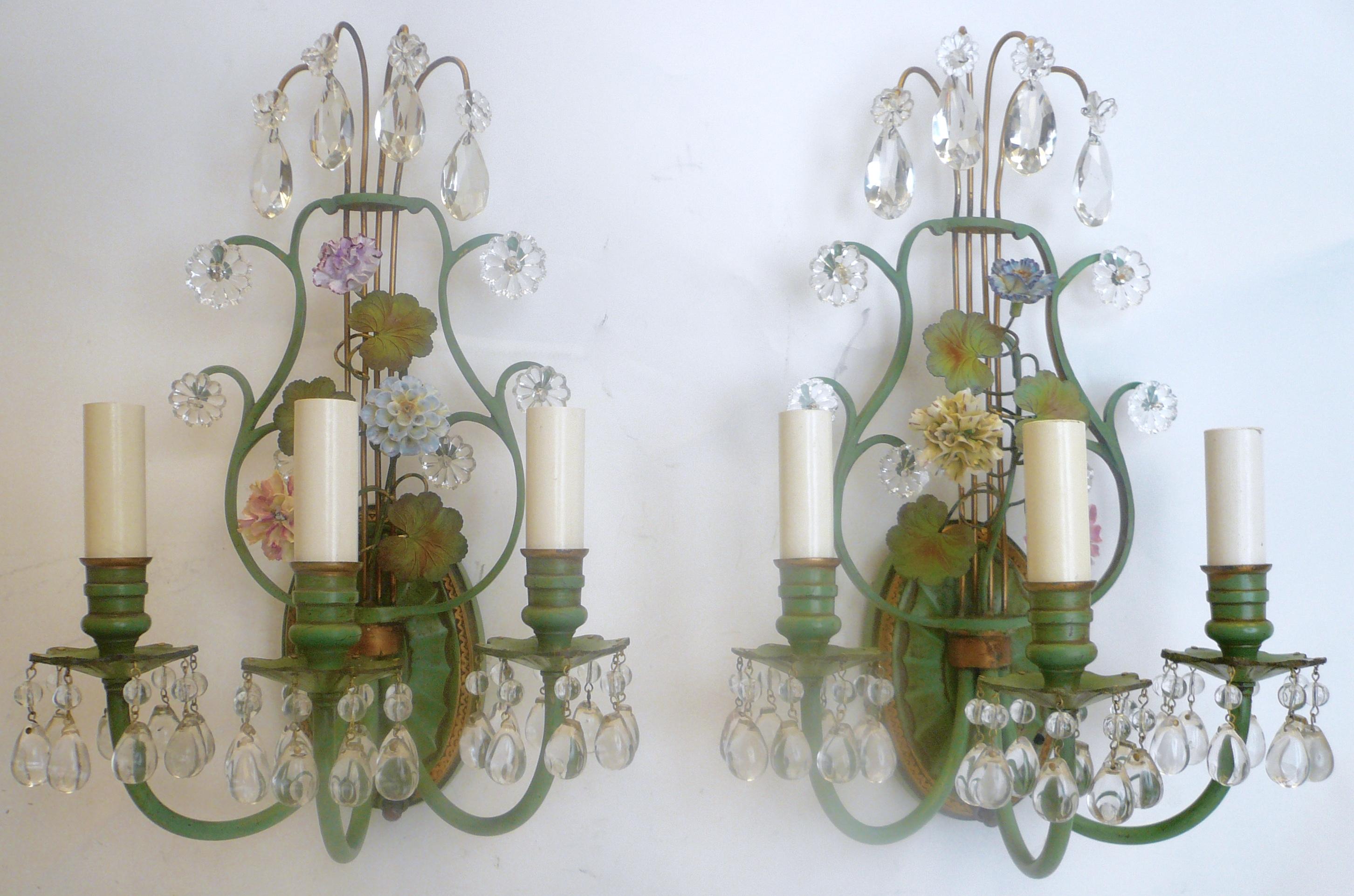 These neoclassical lyre back sconces are in the Louis XVI style, and feature hand painted porcelain flowers. They are made of enameled bronze with gilt highlights, and are hung with crystal drops. These sconces were purchased from the estate of Drue