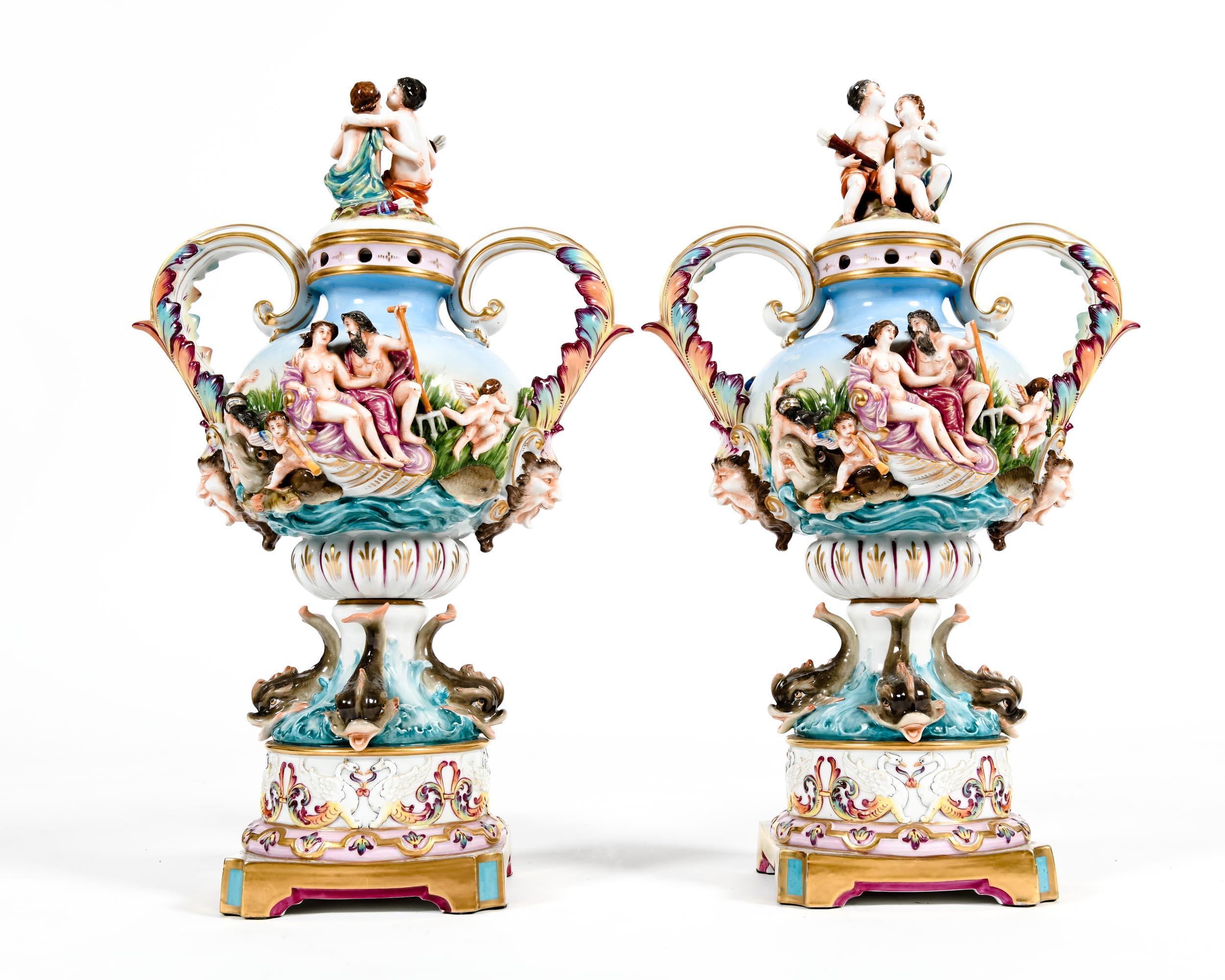 Pair of porcelain covered urns / decorative pieces decorated with exterior bacchantic design detail scenes. Each piece is in excellent antique condition. Minor wear consistent with age / use. Maker's mark blue crowned “N