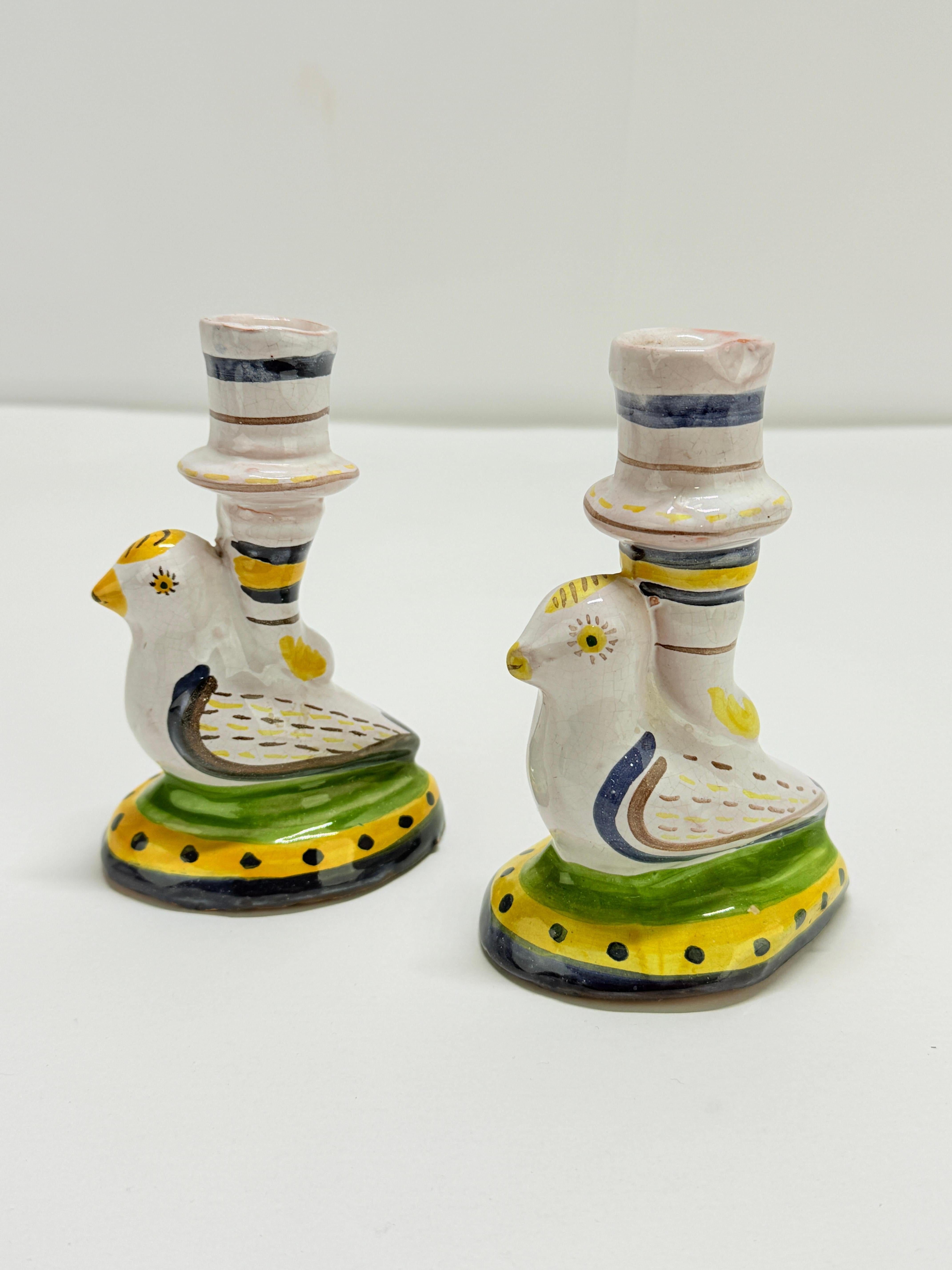 A spirited pair of hand-painted faience candlesticks from Portugal, produced as an authorized reproduction of an earlier historic ceramic type. Each takes the form of a plump, stylized bird perched on an oval base, its back rising into a stacked