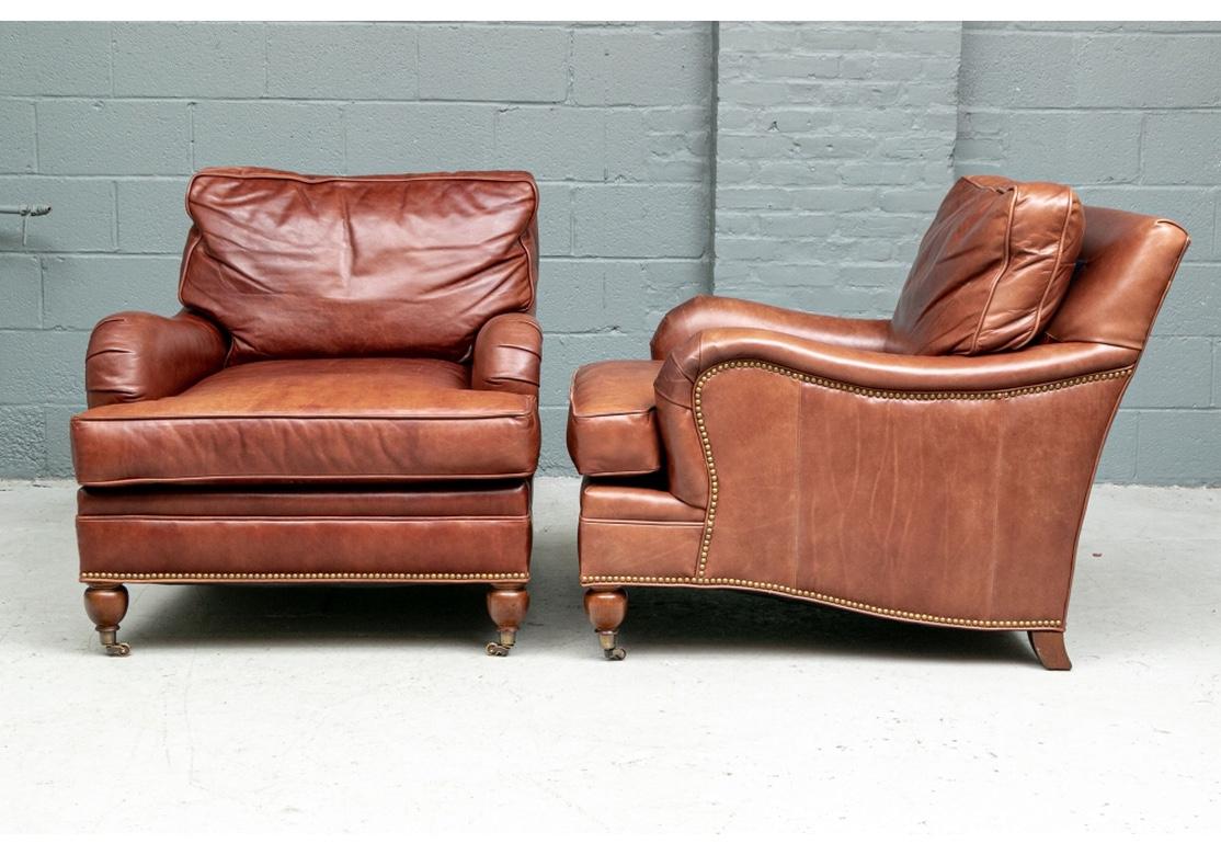 Quality brown leather club chairs with deep seats, sightly sloping backs and rolled pleated arms, the sides made in sections. The back cushion with velcro to keep it in place. Nail head trim along the curved sides and skirt. Raised on brown turned