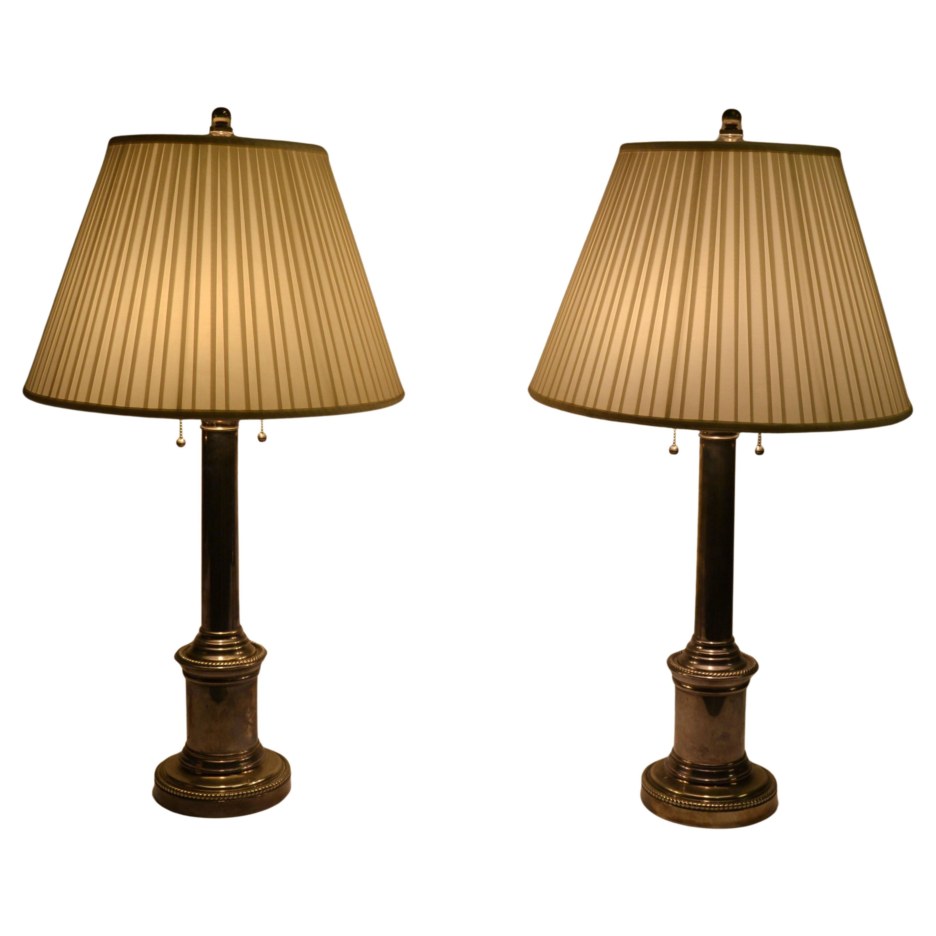 Paire de lampes de table en forme de colonne toscane, fabriquées en laiton massif argenté et ornées de motifs architecturaux au sommet et à la base.
La silhouette robuste est associée à un abat-jour en soie plissée, et chacune est dotée d'une double