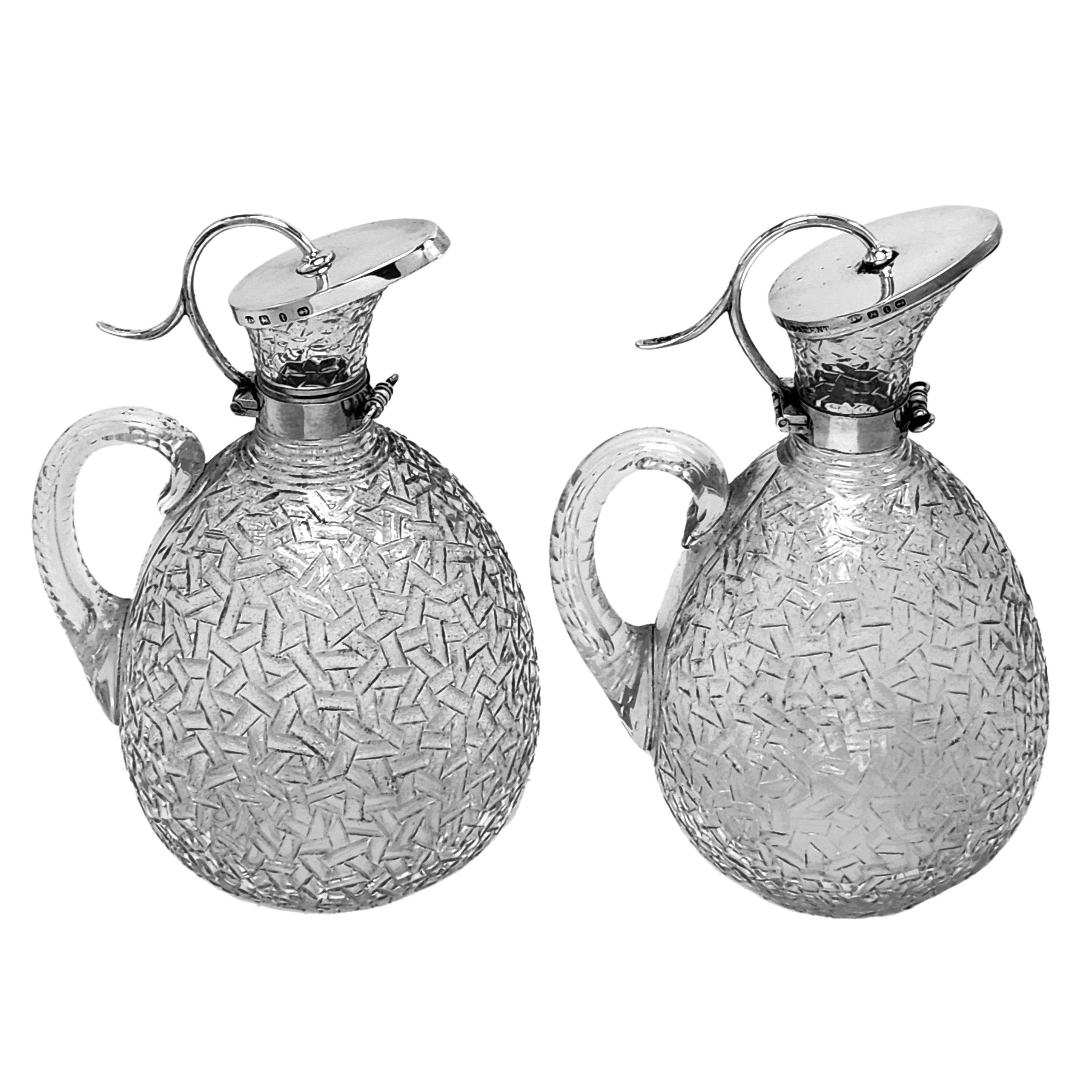 Una coppia di antiche caraffe d'argento vittoriane con corpi in vetro tagliato dai motivi insoliti ed eleganti collari e coperchi d'argento. Queste brocche da vino vittoriane hanno un design che richiama lo stile di Christopher Dresser e delle sue