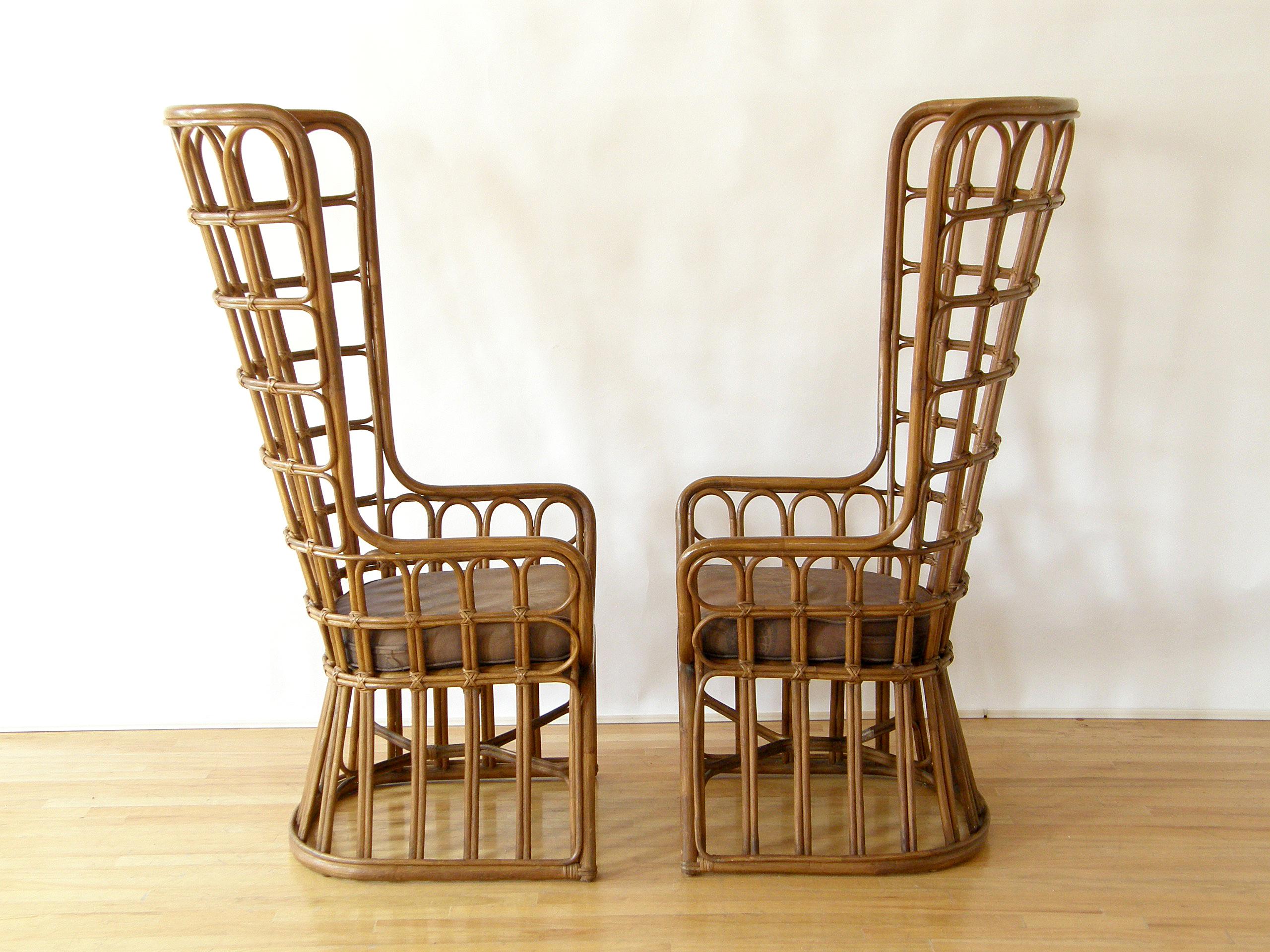 This pair of high back, rattan armchairs has a dramatic presence and a throne-like quality. The chairs are a more modern take on the traditional peacock chair. They have loose cushions and a simplified, fan-shaped back that curves around the sides