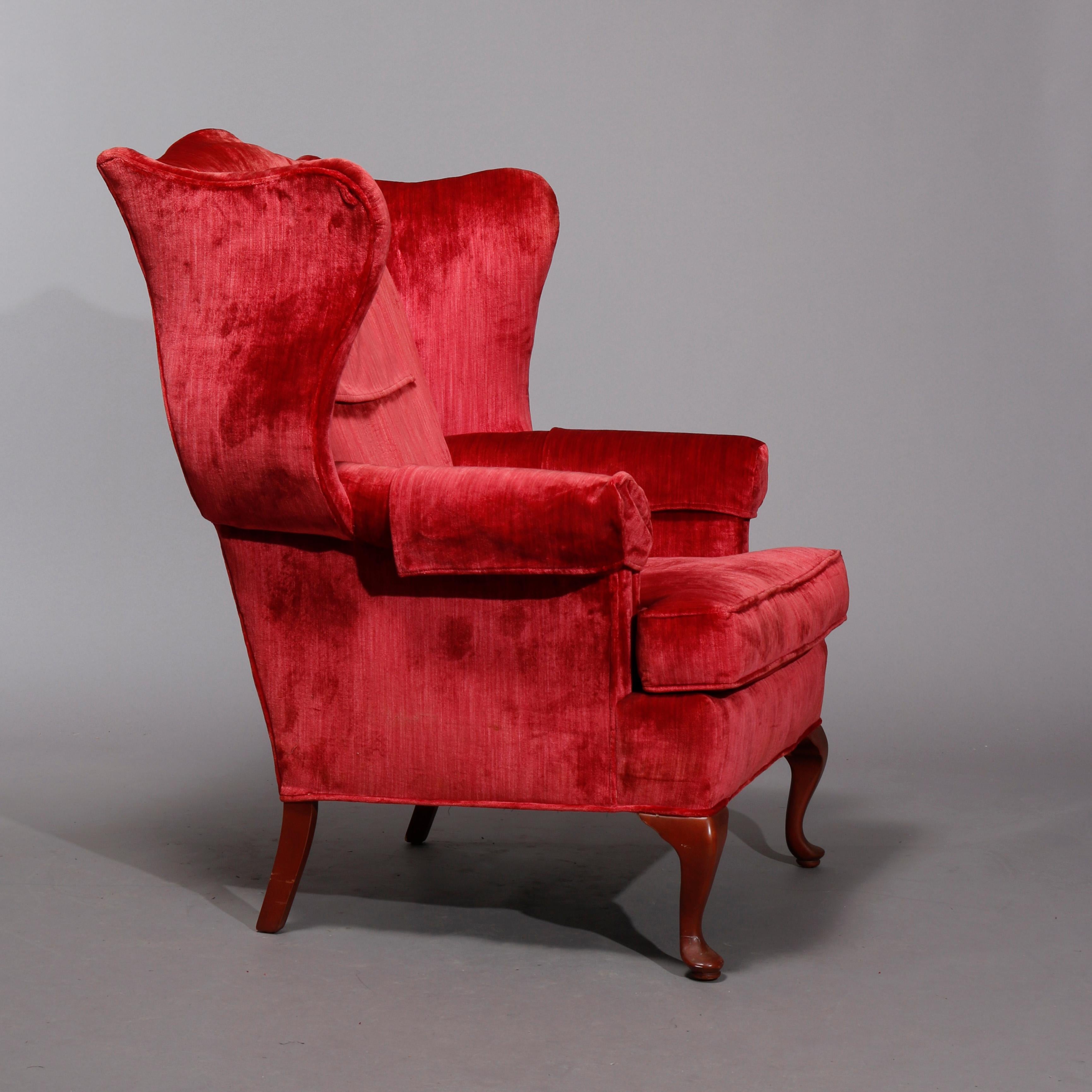 An antique pair of fireside wingback chairs offers shaped backs and scroll form arms with red crused velvet upholstery raised on Queen Anne style mahogany legs, 20th century

Measures: 44.5