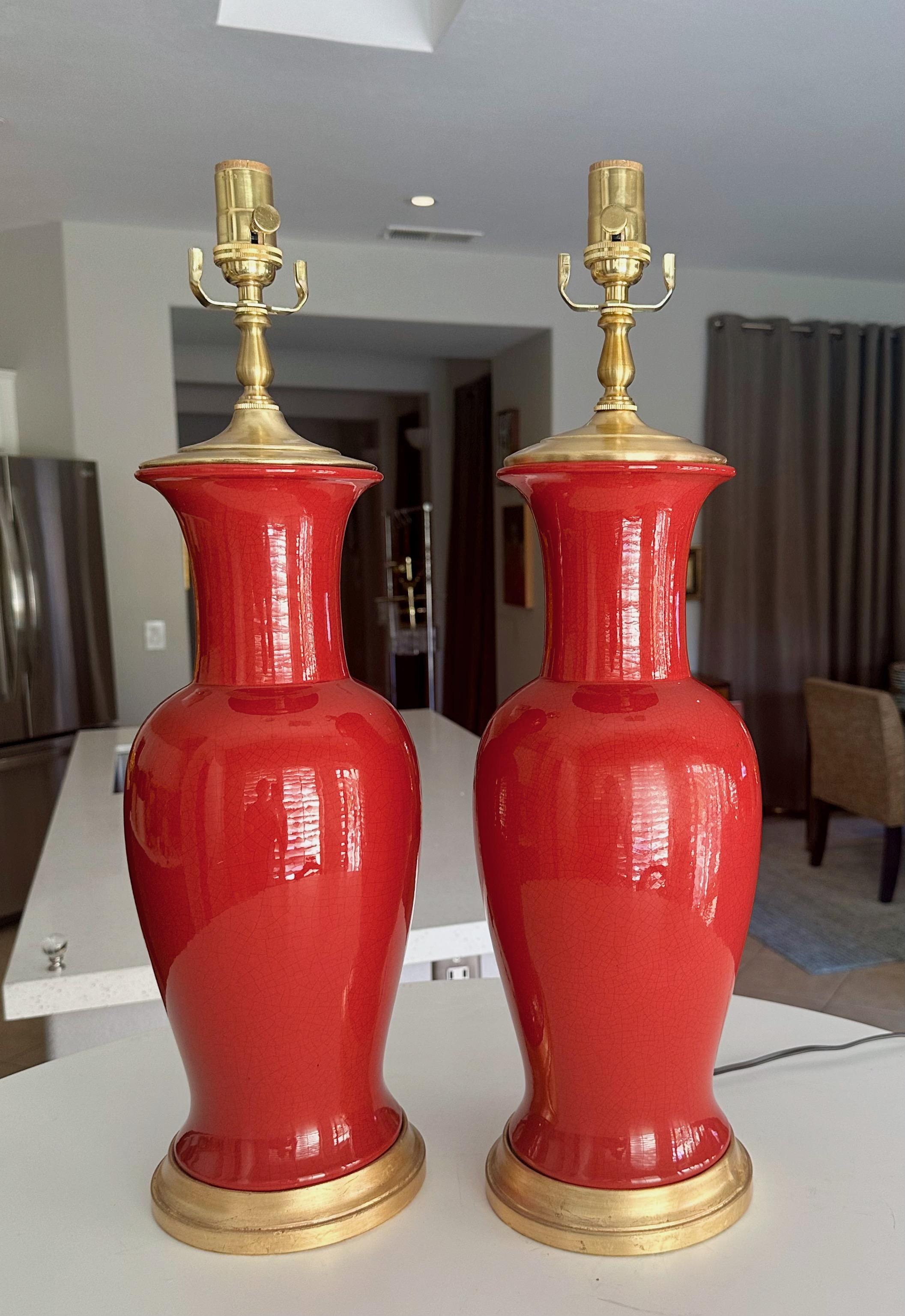 Paire de lampes de table en céramique de style asiatique, de forme balustre et de couleur orange rougeâtre, sur des bases en bois doré. Le câblage a été refait à neuf avec des prises à 3 voies en laiton et des cordons. Les abat-jour ne sont pas