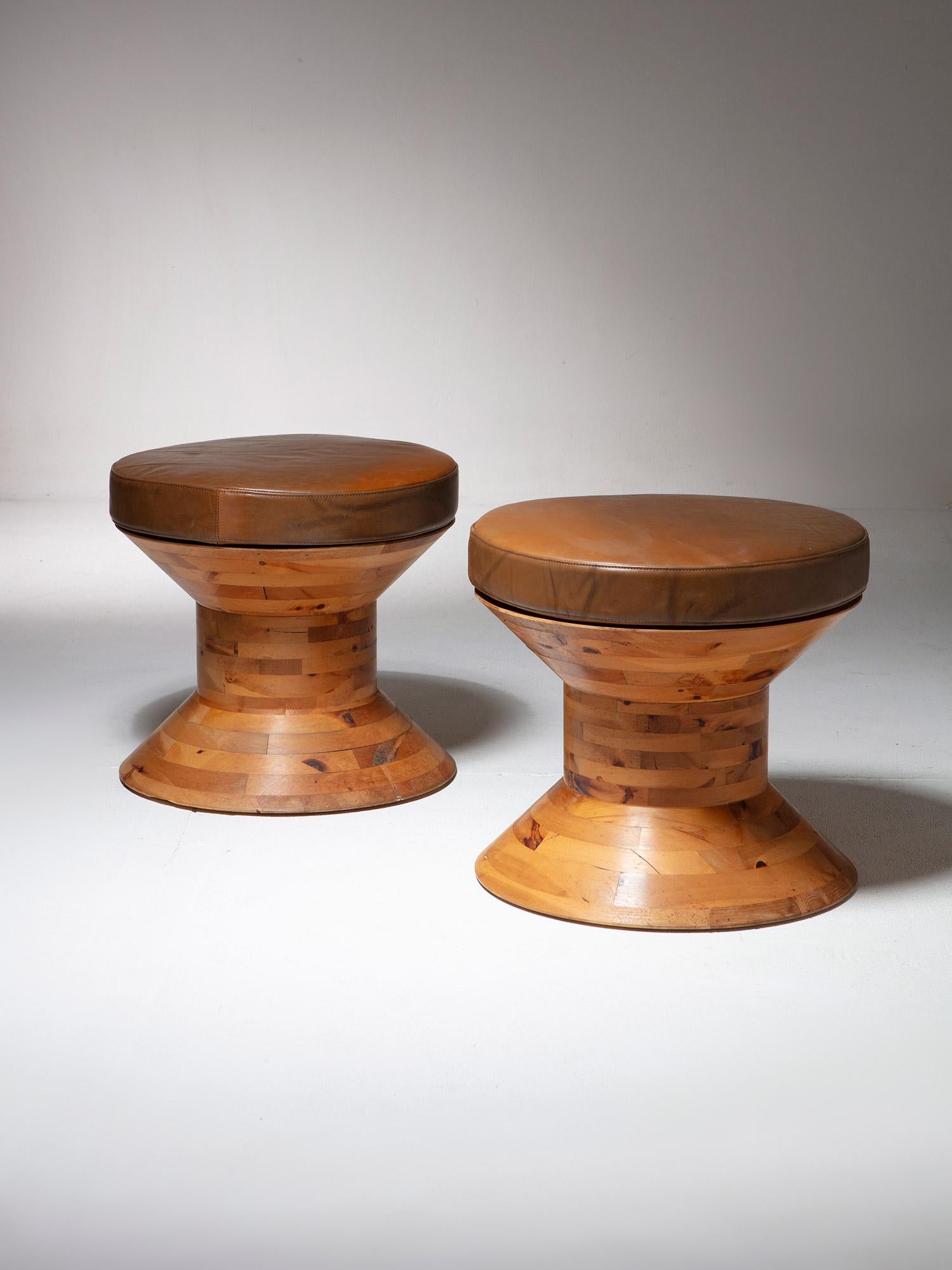 Paire de tabourets en bois massif en forme de bobine.
Coussins mobiles recouverts de cuir, pieds en acier sur la base pour préserver le bord arrondi coupé. 
Deux ensembles disponibles, prix par ensemble.