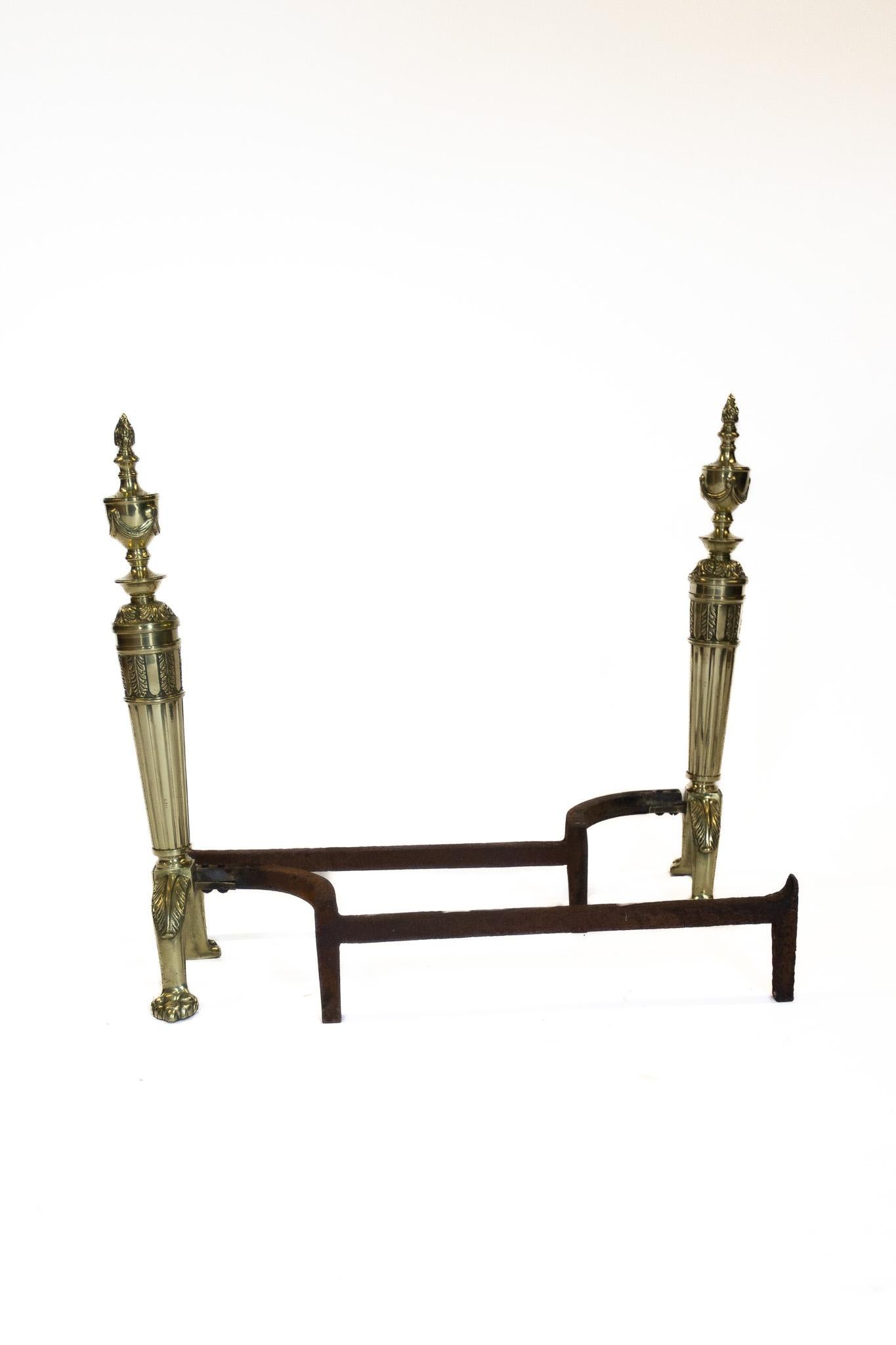Pair Regency Zeitraum gegossen Messing Andirons, 
nach dem Vorbild von Robert Adam,
Gegossenes Messing mit Flambe-Finials, Swags & Reeded Detail
Sitzend auf bogenförmiger Front mit Krallenfüßen, 
Tragendes Eisengestell zur Aufnahme des Feuerrostes,