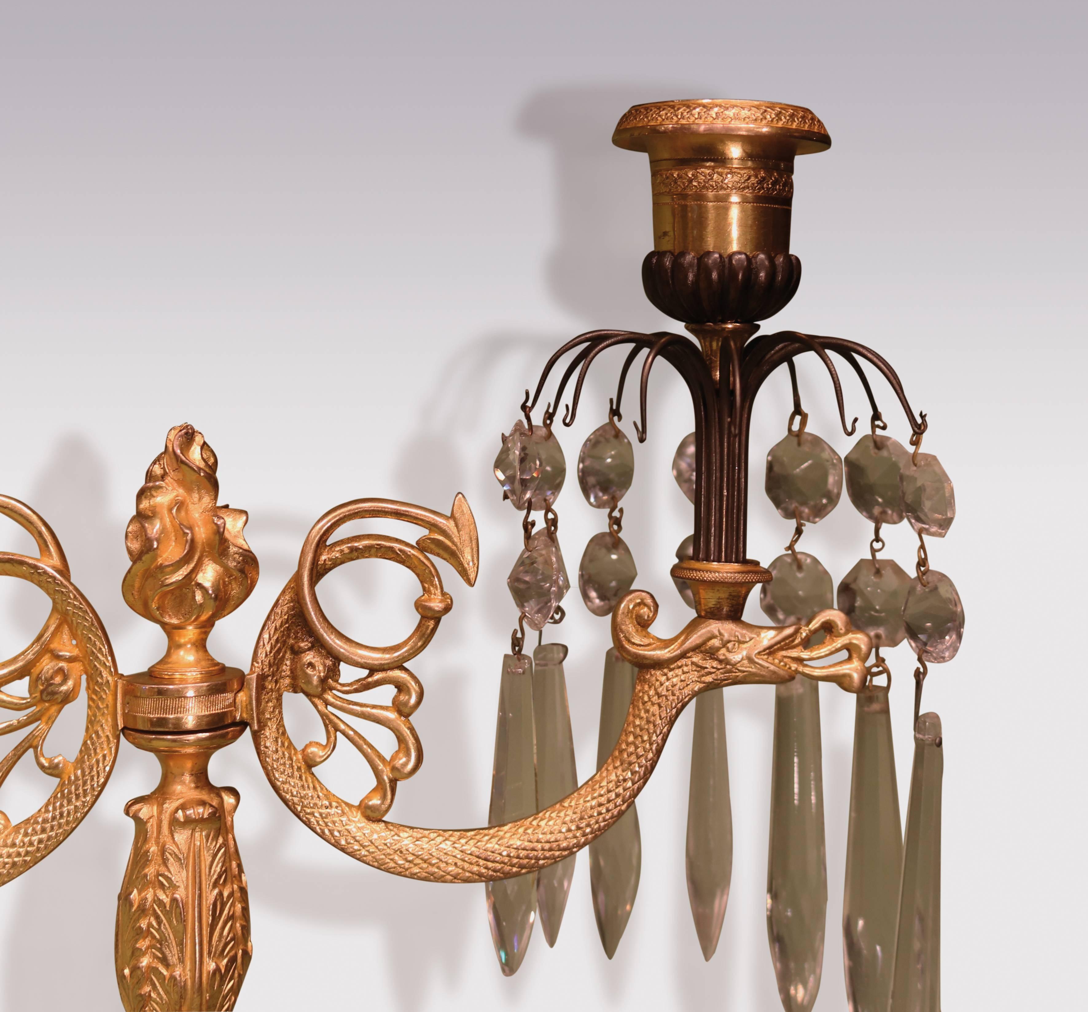 A pair of early 19th century Regency period bronze and ormolu two-light lustre candlesticks, having engine turned nozzles, above scroll serpent branches with honeysuckle decoration, raised on acanthus turned stem with flame finial, above triple