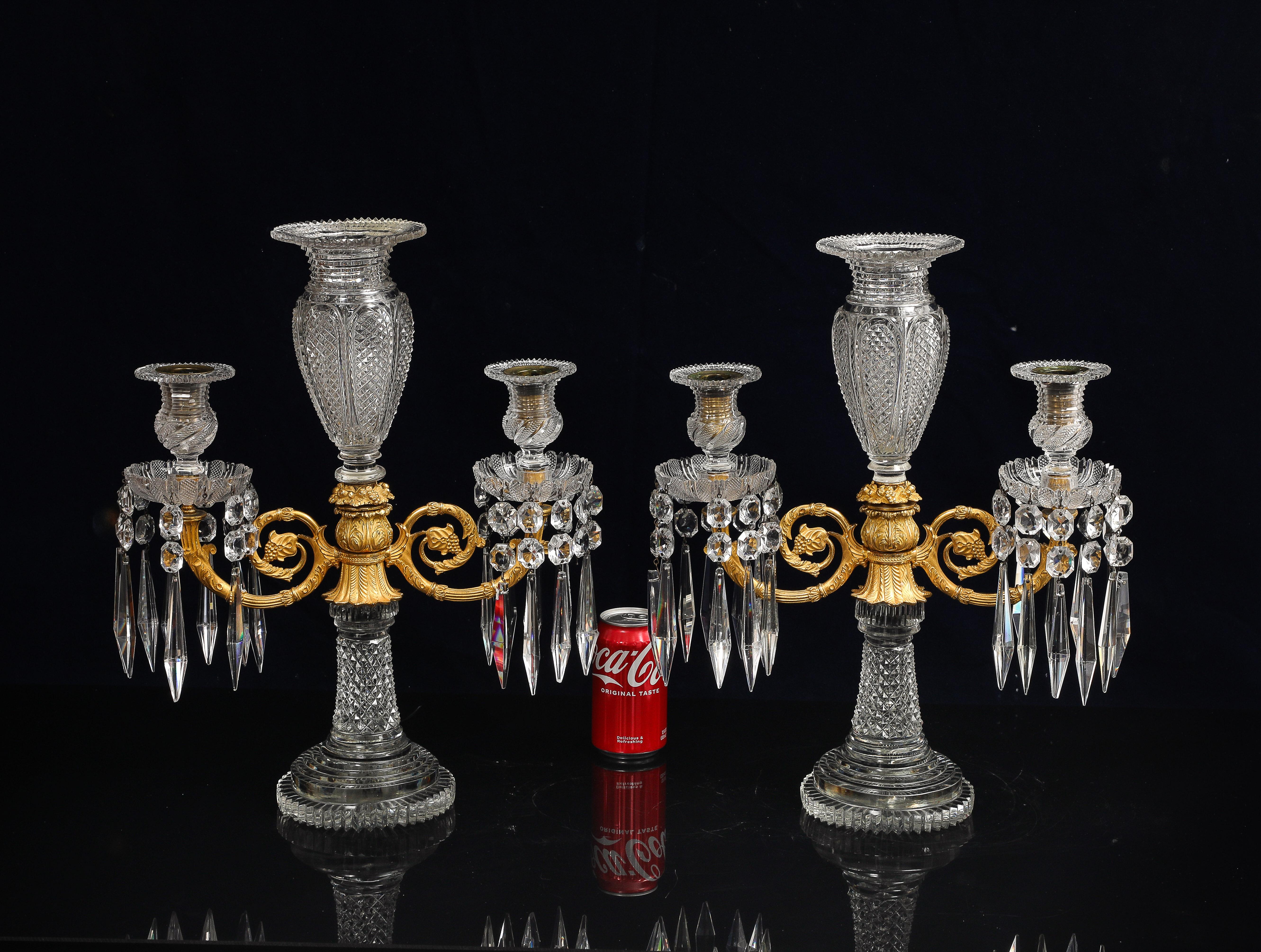 A Pair of Regency Crystal and Gilt Bronze Two-Light Candelabra with Central Crystal Vase, Attributed to John Blades, London, circa 1810. Each features a central urn-shaped crystal stem with fine diamond-cut panels, tapering to a stepped circular