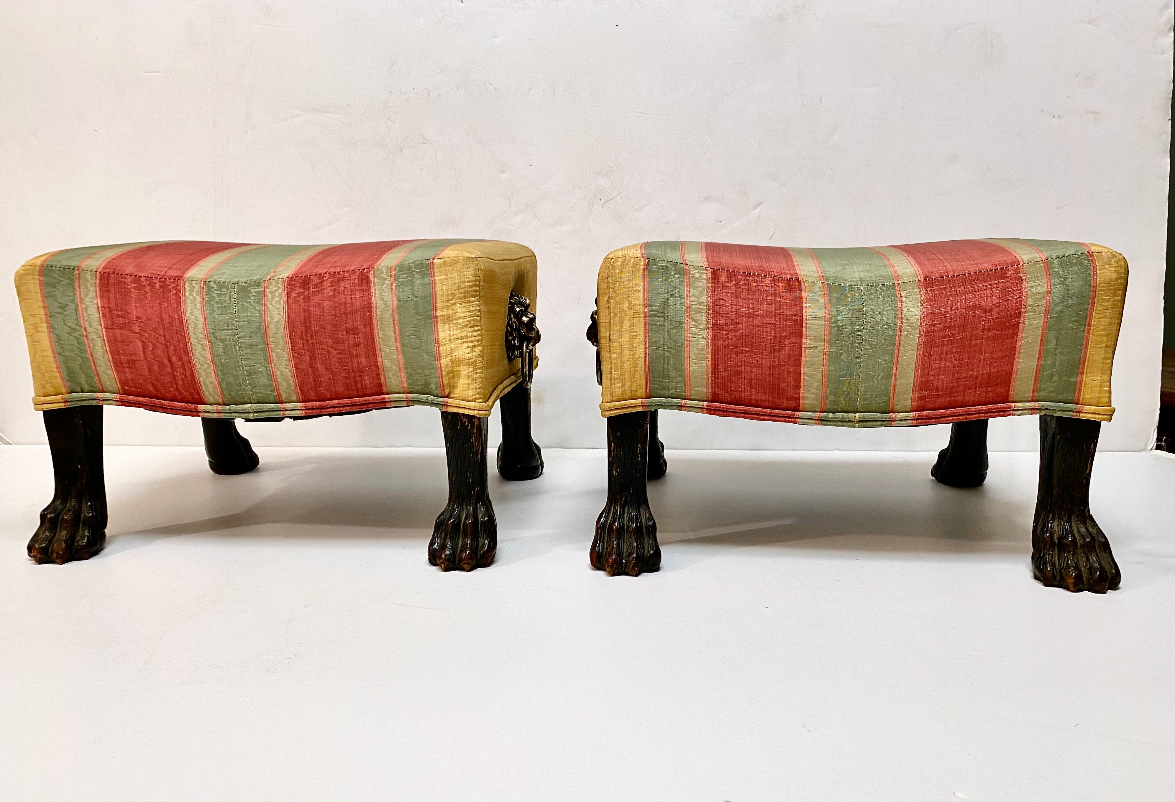 This is a unique pair of period Regency foot stools that features beautifully carved hairy paw feet and finely cast lion head side handles. The stools are in overall very good condition. The upholstery shows some wear, as shown in the photos. We can