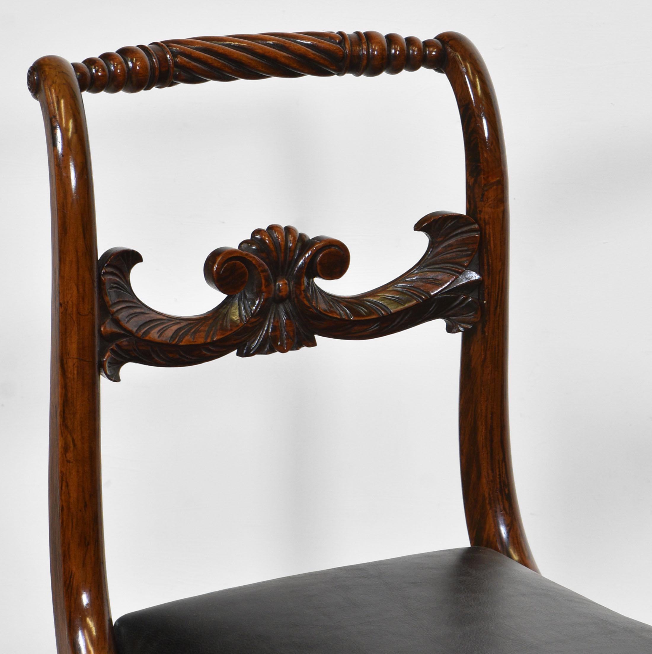 A pair of Regency scroll back chairs in simulated rosewood and black leather inset seats. Circa 1820.

The chairs have a rope twist turned top rail, with a carved central rail, and terminate on sabre front legs. National pride in the British naval