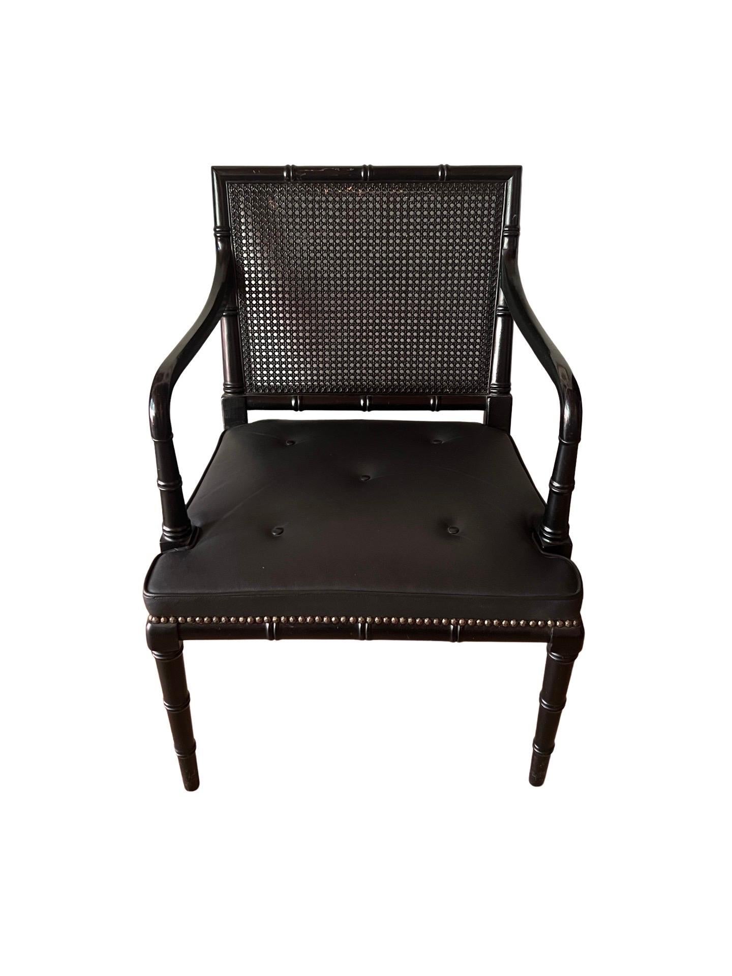 English, 20th century. 
A vintage pair of English bench made armchairs. Each with a faux bamboo Regency style frame which is done with an ebony finish. The seats have recessed button accents and have a cane back. Unmarked. 
