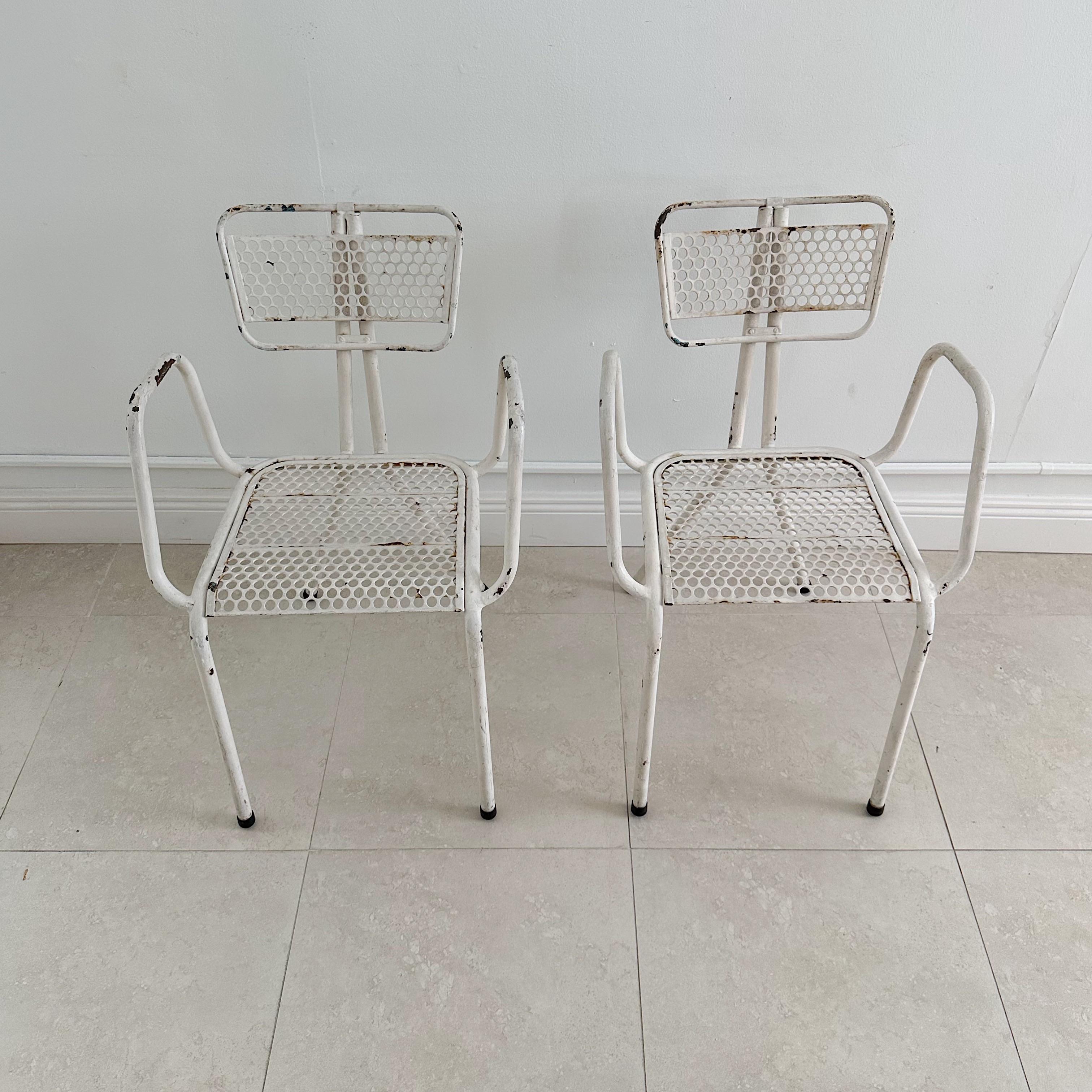 A pair of vintage metal arm chairs designed by René Malaval for Bloc Metal France. Quite rare to find these chairs with arms.  These post-war chairs feature a painted white finish with perforated metal backrests and seats. The chairs retain the old